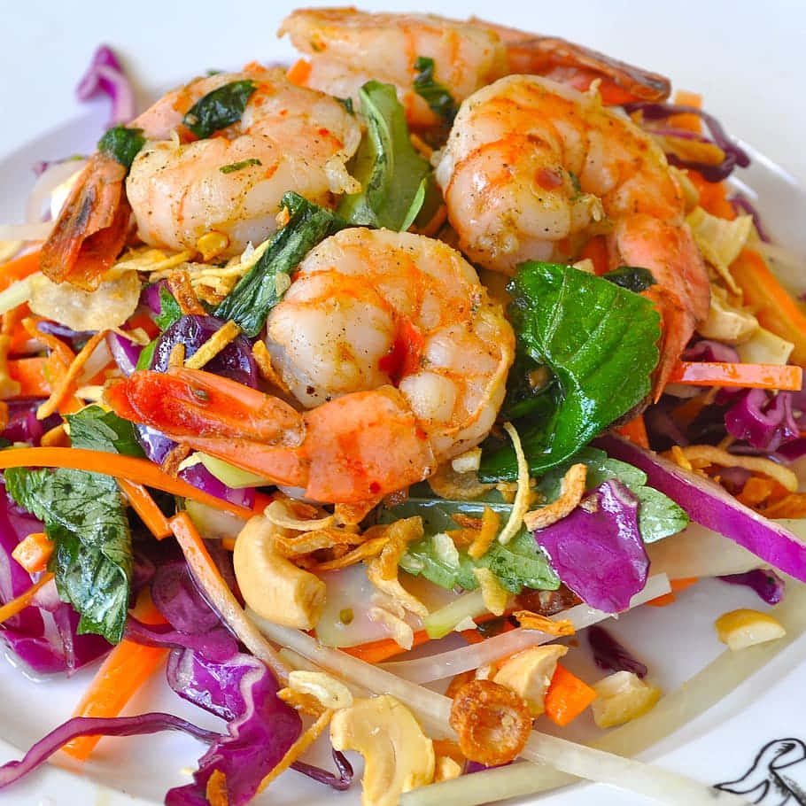 shrimp 桌布 壁紙 — 一個充滿活力的特寫，展示一盤辛辣蝦沙拉，搭配紫甘藍、橙色胡蘿蔔和腰果，盛放在白色盤子上。