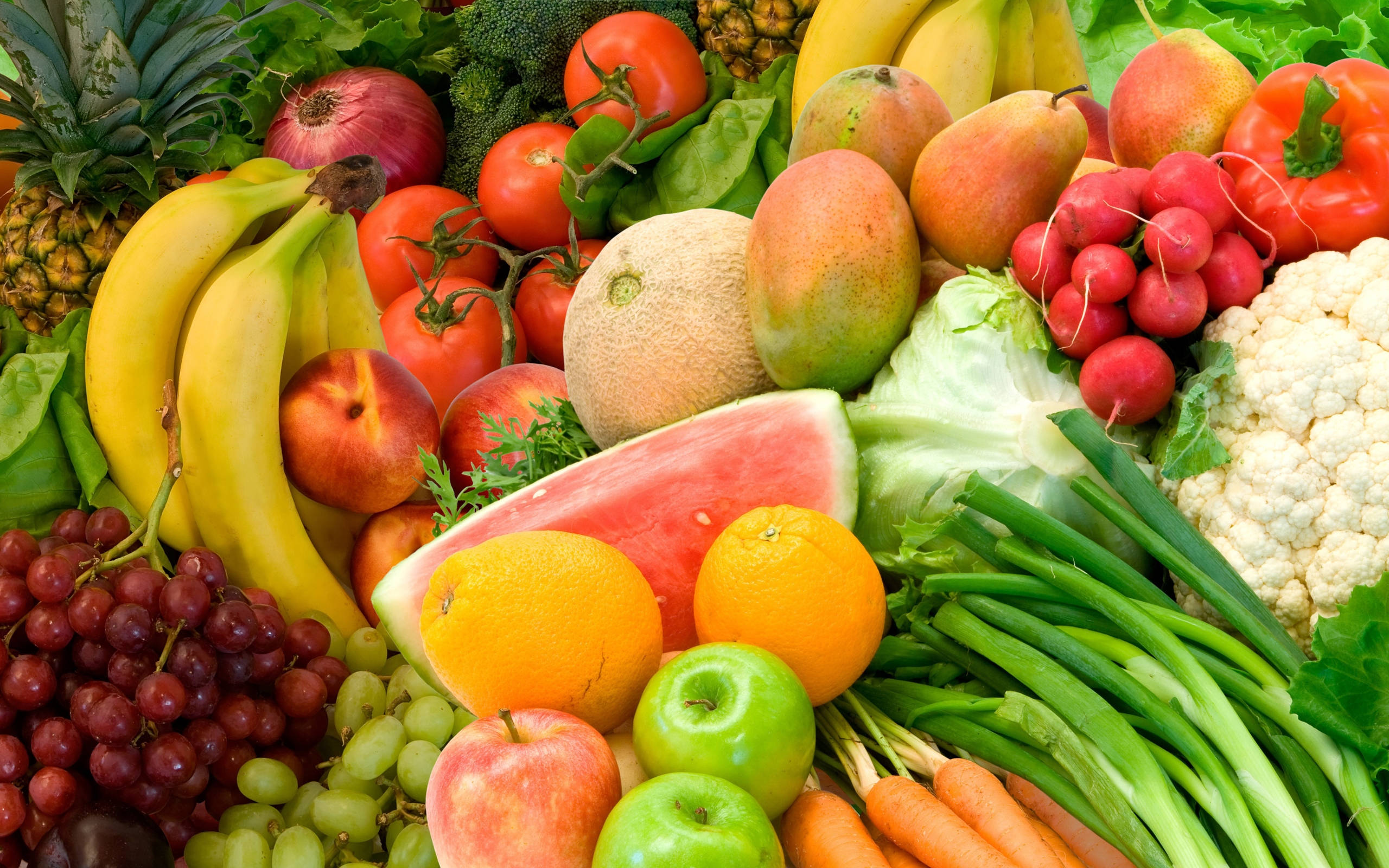 Fruits 桌布 壁紙 — 一個充滿活力的特寫，展示了各種新鮮水果和蔬菜，包括香蕉、西瓜、葡萄和胡蘿蔔，排列成色彩繽紛且豐富的一堆。