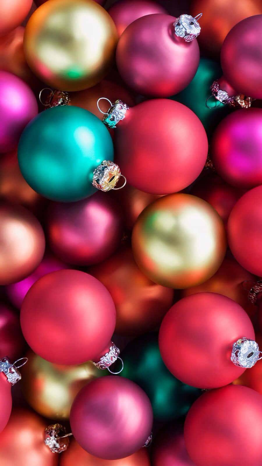 Christmas Cell Phone 桌布 壁紙 — 一個充滿活力的特寫，展示了帶有銀色蓋子的光澤紅色、粉紅色和藍綠色聖誕裝飾品堆疊在一起。
