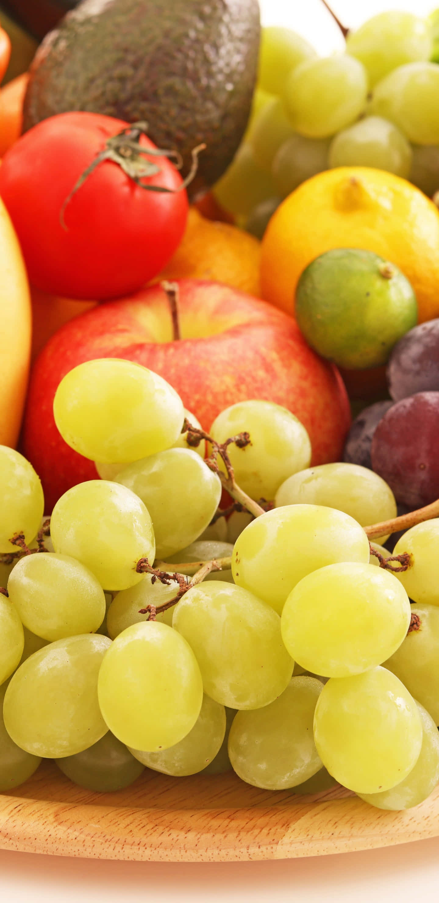 Fruits 桌布 壁紙 — 一個充滿活力的特寫，展示各種新鮮水果，包括青葡萄、酪梨、番茄和柑橘，擺放在木盤上。