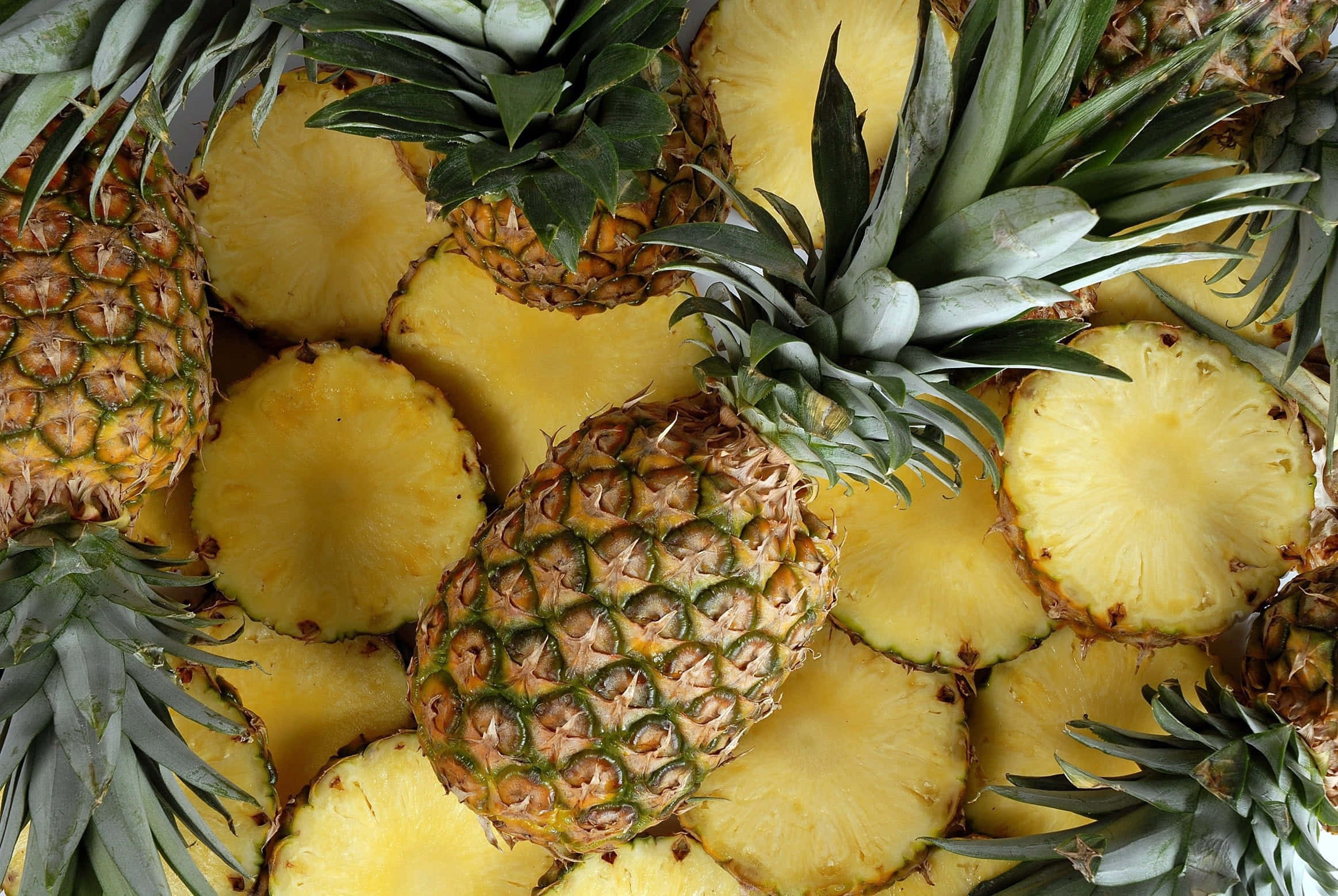 Pineapple 桌布 壁紙 — 一個充滿活力的特寫，展示完整和切片的鳳梨，呈現多汁的黃色果肉和帶刺的綠色冠部。
