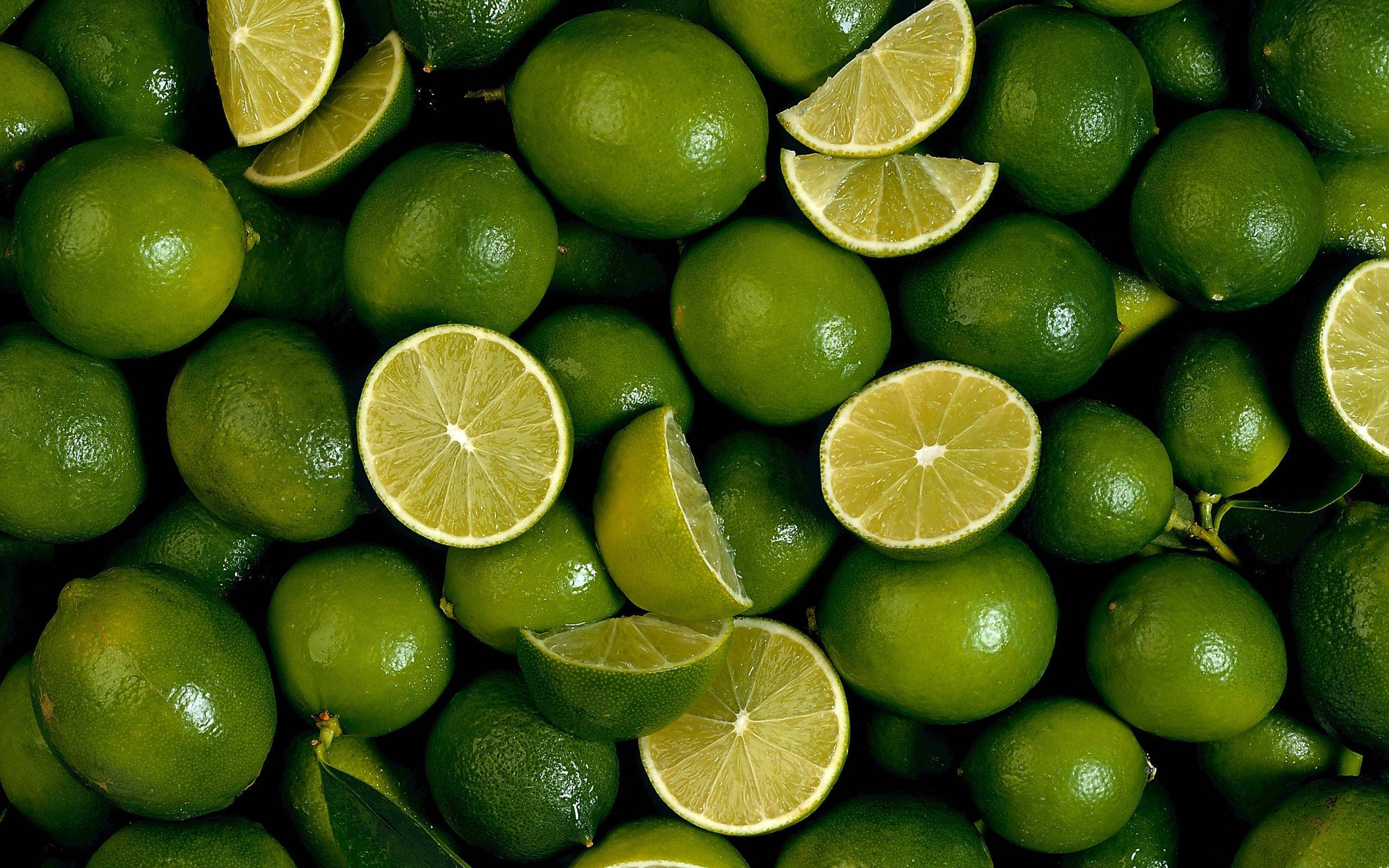 Fruits 桌布 壁紙 — 一個充滿活力的特寫，展示完整和切片的青檸，帶有光澤的表皮和多汁的果肉。