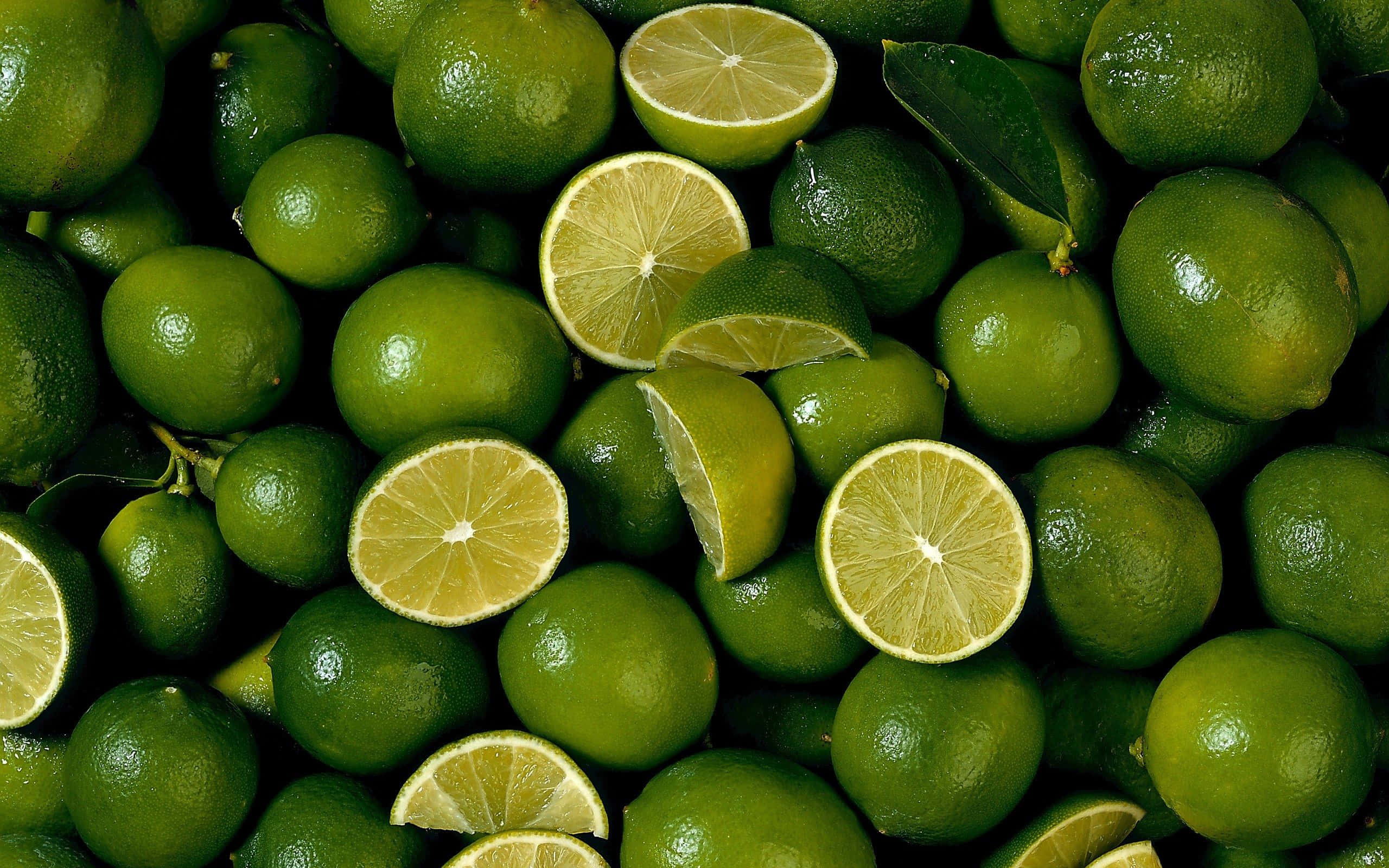 Lime 桌布 壁紙 — 一個充滿活力的特寫，展示完整和切片的青檸，表皮光滑，果肉多汁呈黃色。