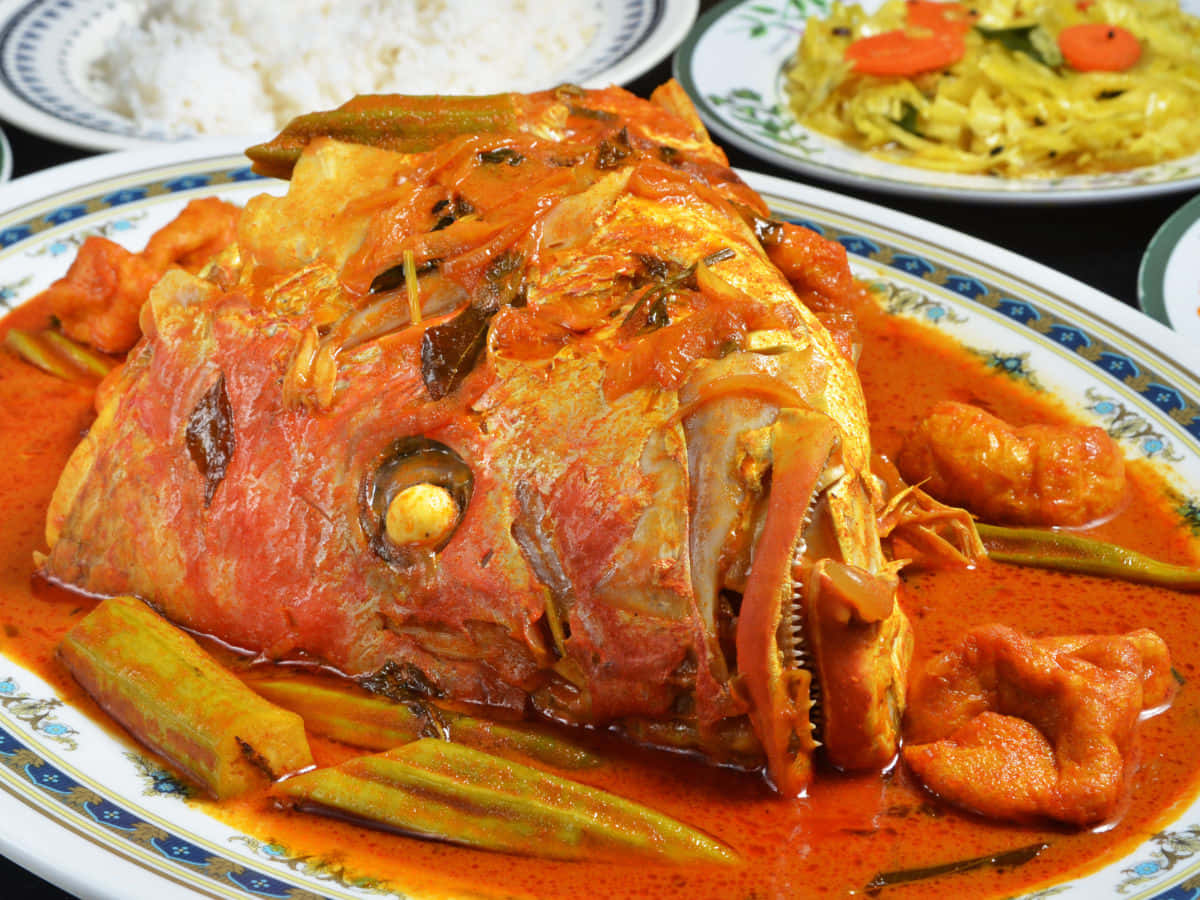 Food Photography 桌布 壁紙 — 一個充滿活力的特寫，展示整個魚頭浸泡在濃郁的紅咖哩醬中，背景有秋葵和米飯。