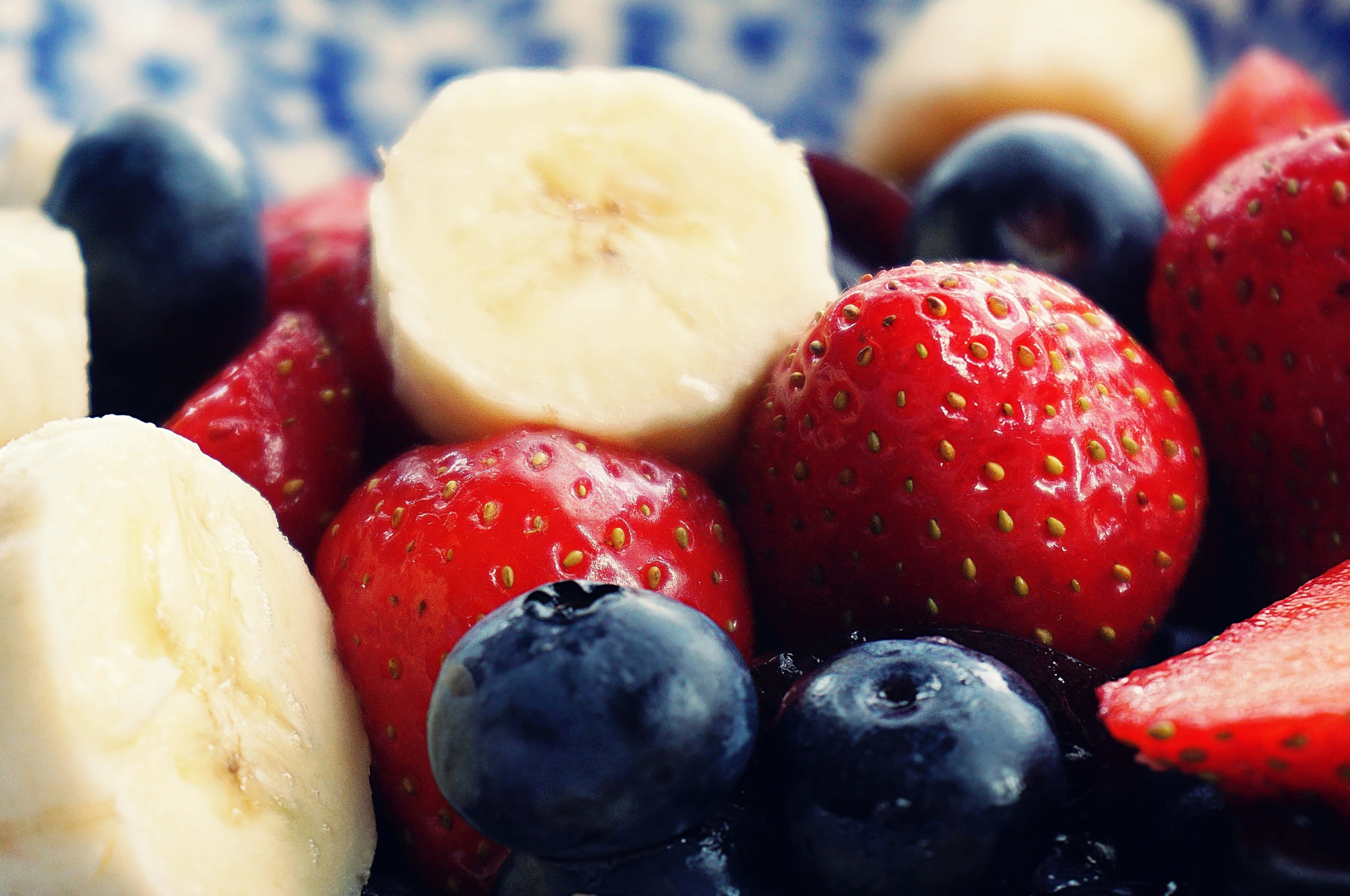 Summer Fruits 桌布 壁紙 — 一個充滿活力的特寫，新鮮切片香蕉、草莓和藍莓整齊排列在一個藍色圖案盤子上。
