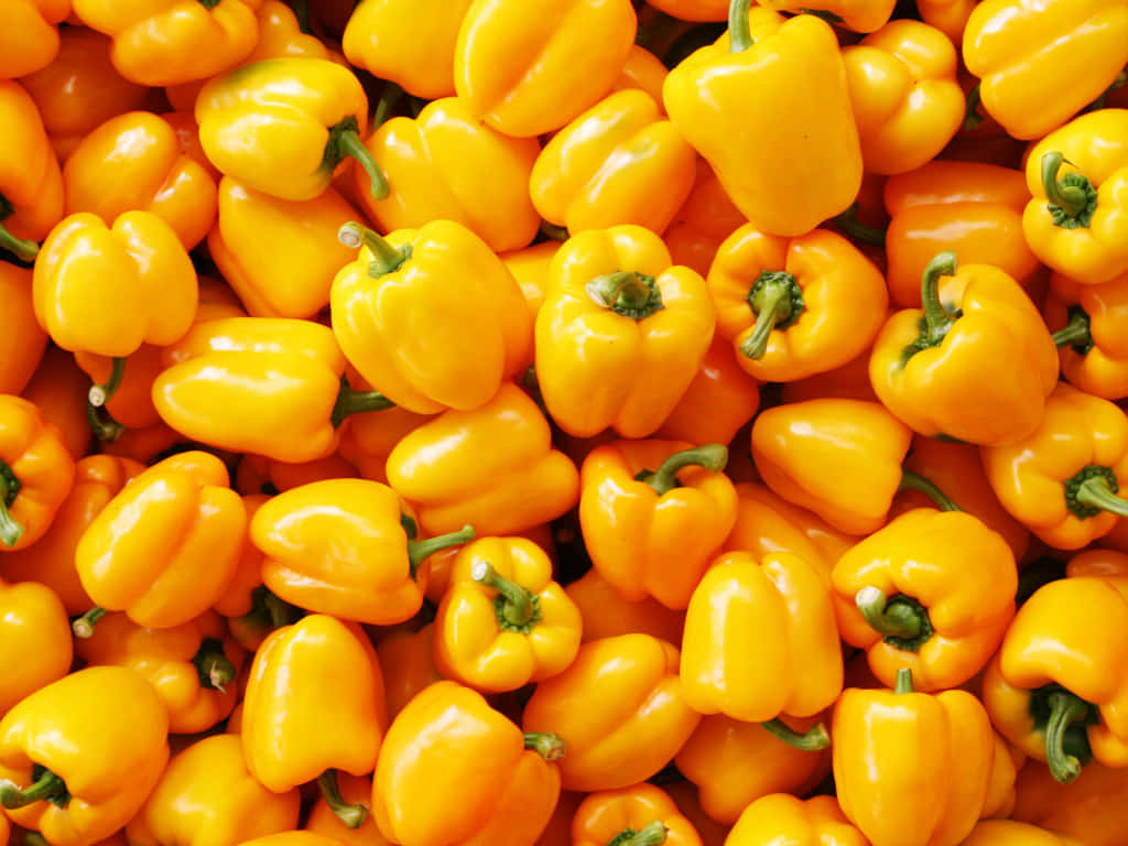 Yellow Bell Pepper 桌布 壁紙 — 一個充滿活力的特寫，閃亮的黃色甜椒與綠色莖堆疊在一起。
