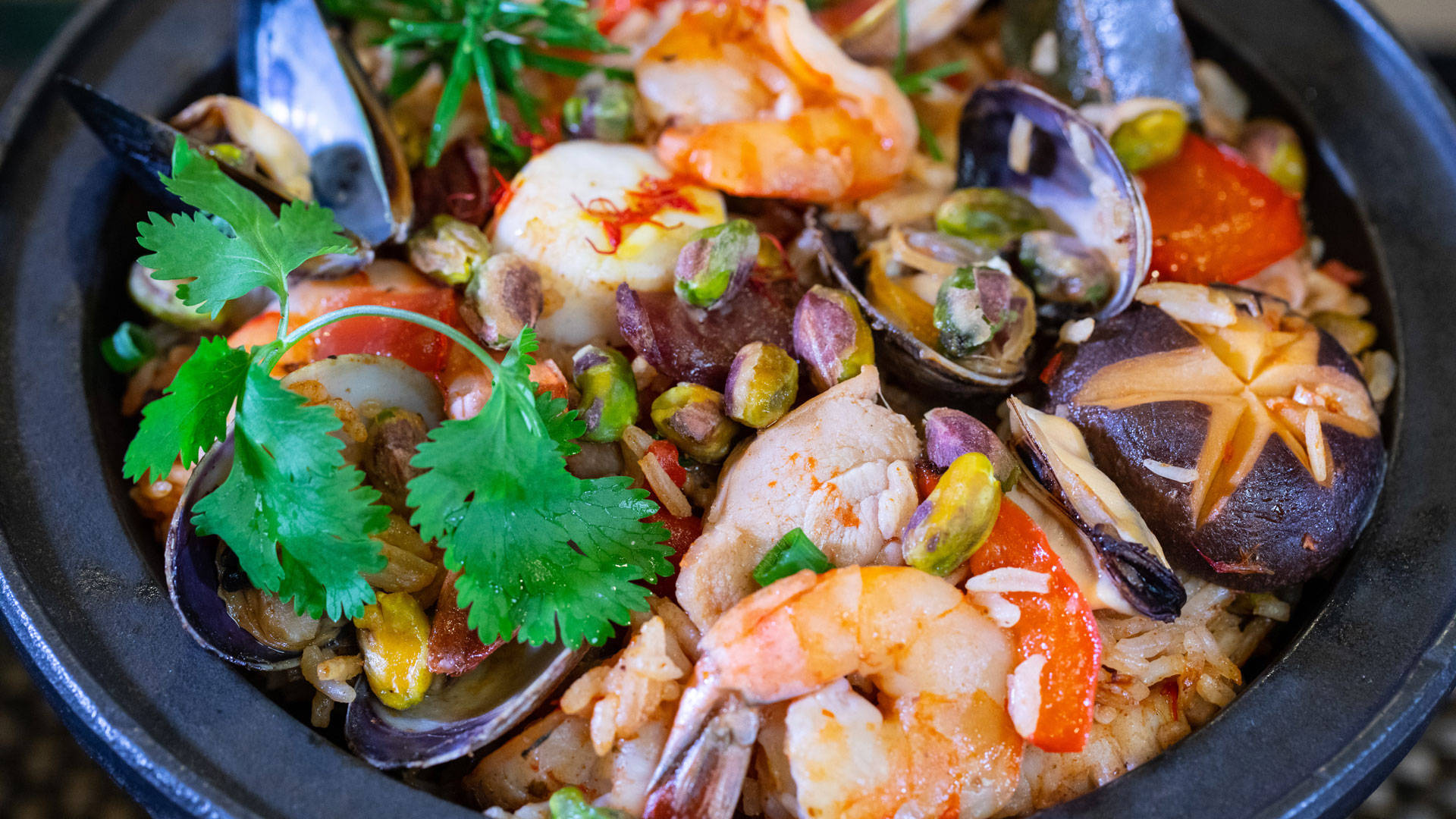 prawn 桌布 壁紙 — 一個充滿活力的特寫鏡頭，展示了一個深色碗中冒著熱氣的海鮮燉飯，裡面滿是蝦、淡菜、豌豆和新鮮香菜。