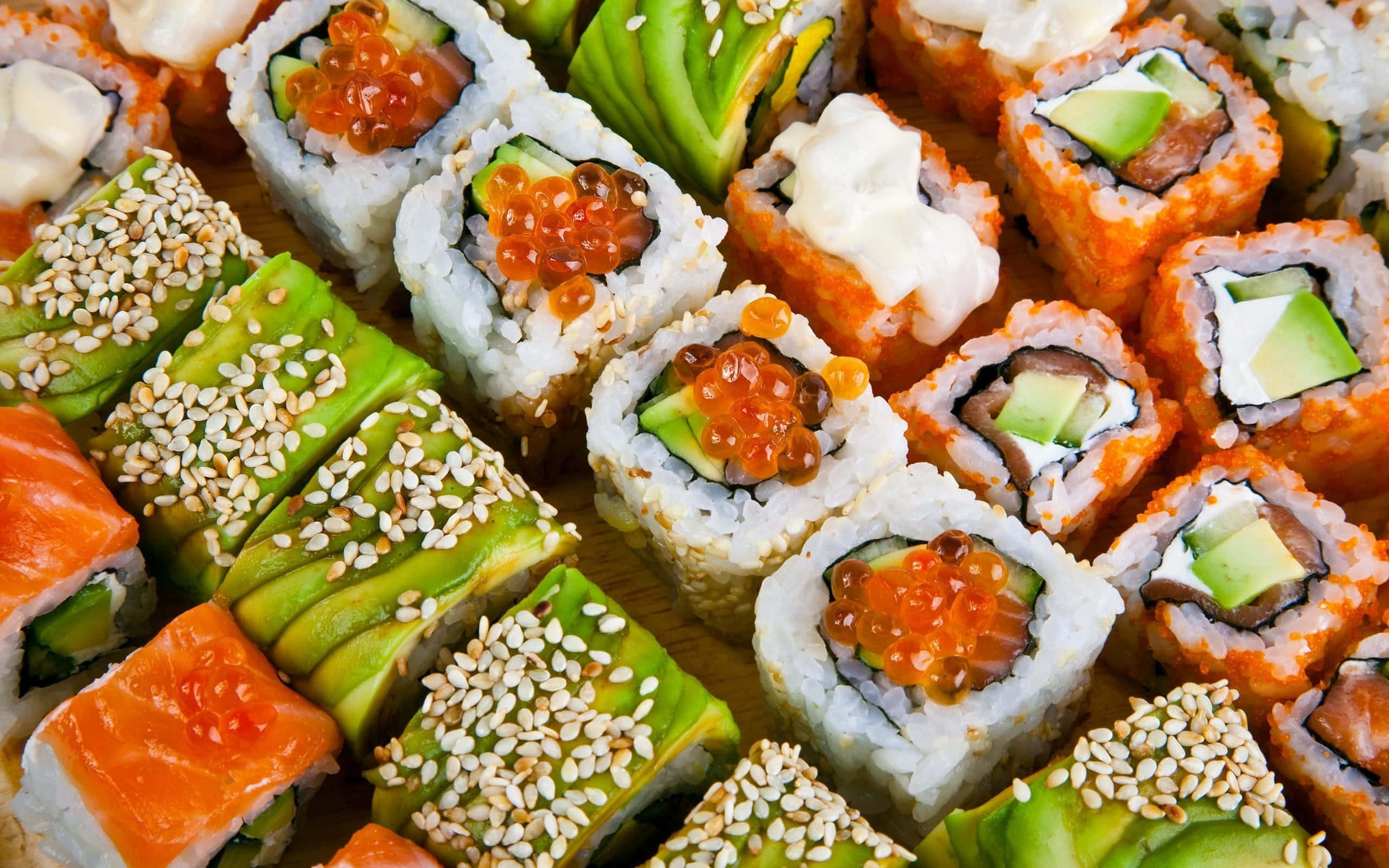 Food Photography 桌布 壁紙 — 一個充滿活力的特寫鏡頭，展示各種壽司卷，上面撒有芝麻、飛魚籽和酪梨，放在木板上。