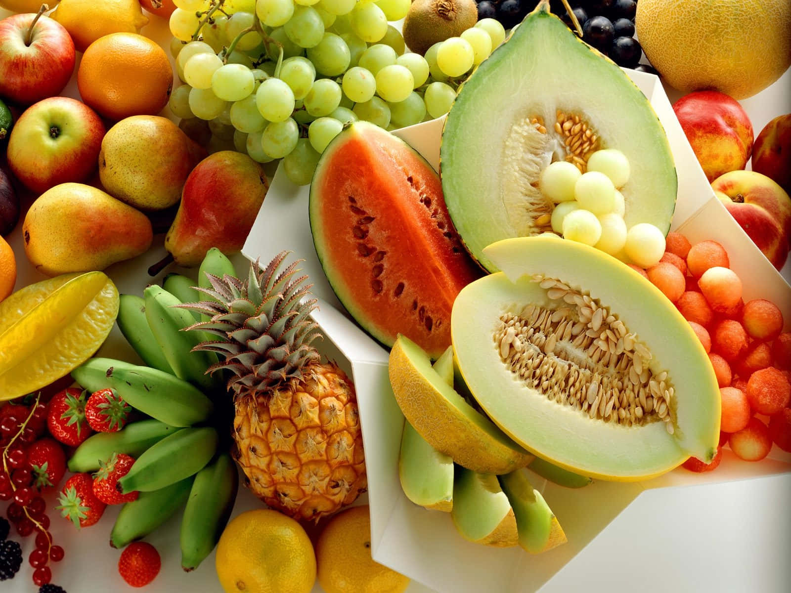 Fruit 桌布 壁紙 — 一個充滿活力的特寫鏡頭，展示各種新鮮水果，如西瓜、哈密瓜、鳳梨和葡萄，整齊排列在一個白色盒子裡。