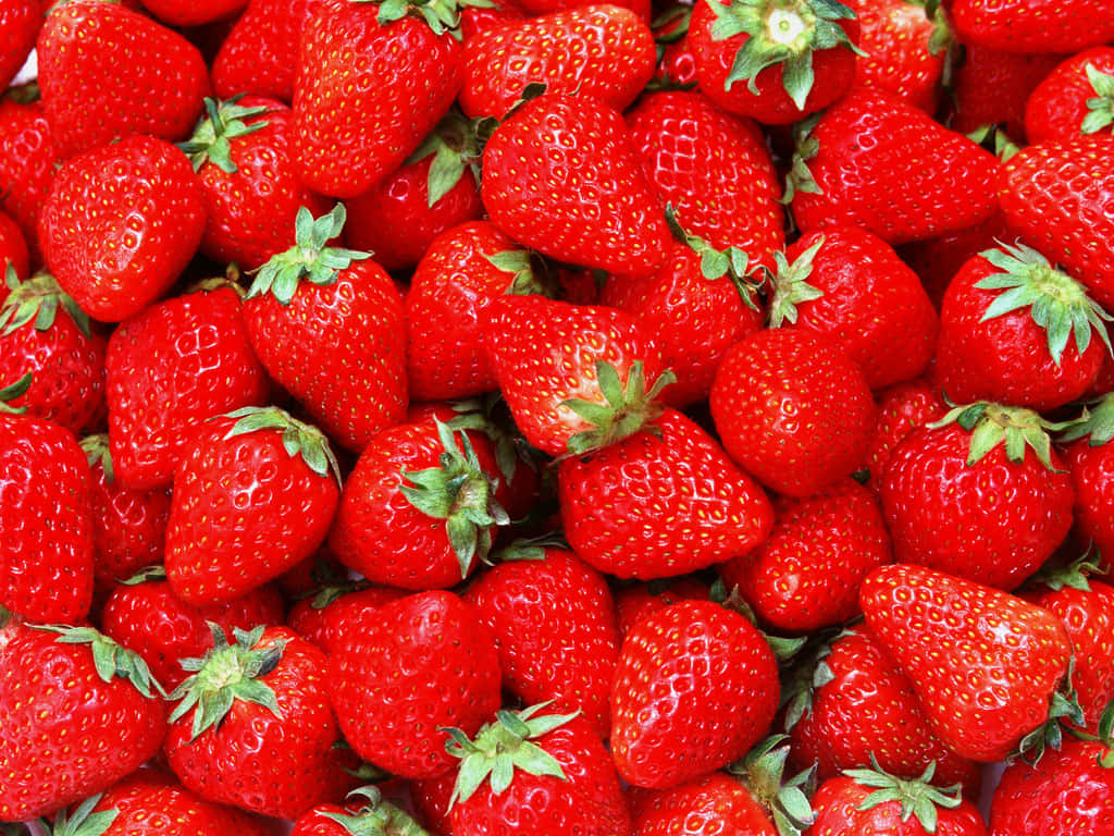 Strawberries 桌布 壁紙 — 一個充滿活力的特寫鏡頭，展示多汁成熟的草莓，帶有綠色頂部堆疊在一起。
