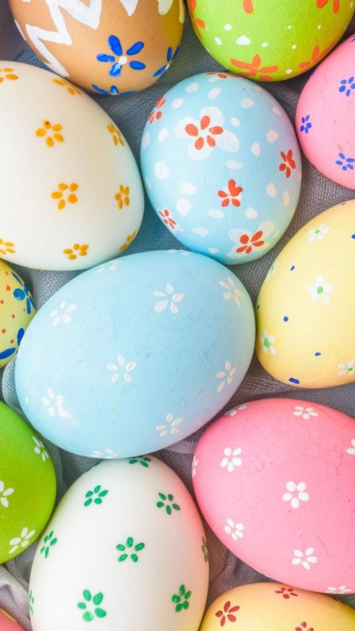 Easter 桌布 壁紙 — 一個充滿活力的特寫鏡頭，展示手繪復活節彩蛋，帶有粉彩花卉圖案，放置在紋理灰色表面上。