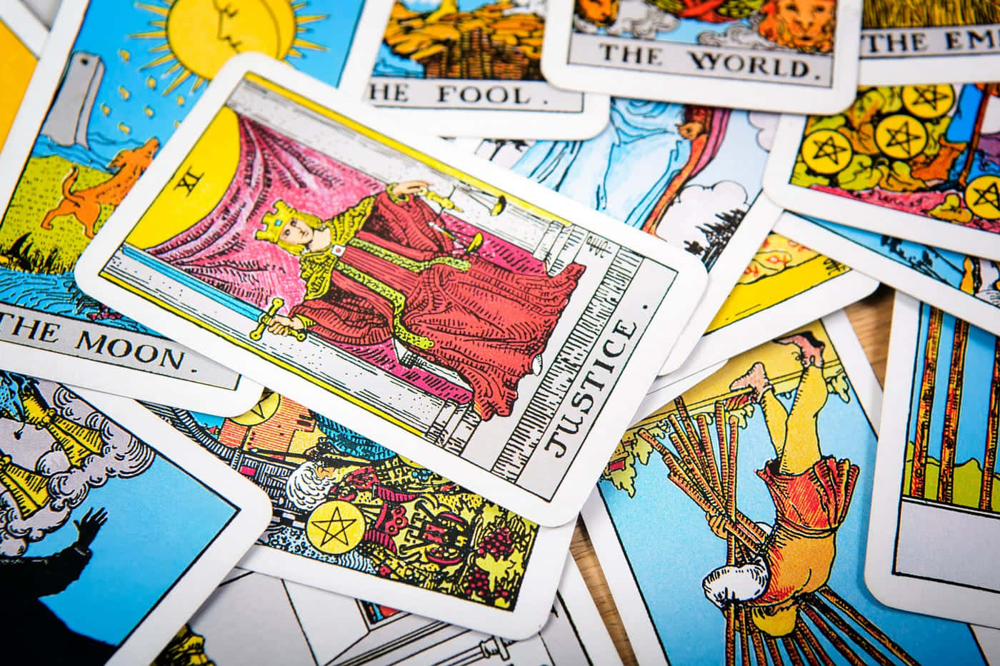 Tarot Card 桌布 壁紙 — 一個充滿活力的特寫鏡頭，展示散落的塔羅牌，其中「正義」牌醒目地放在「愚者」和「月亮」等其他牌之上。