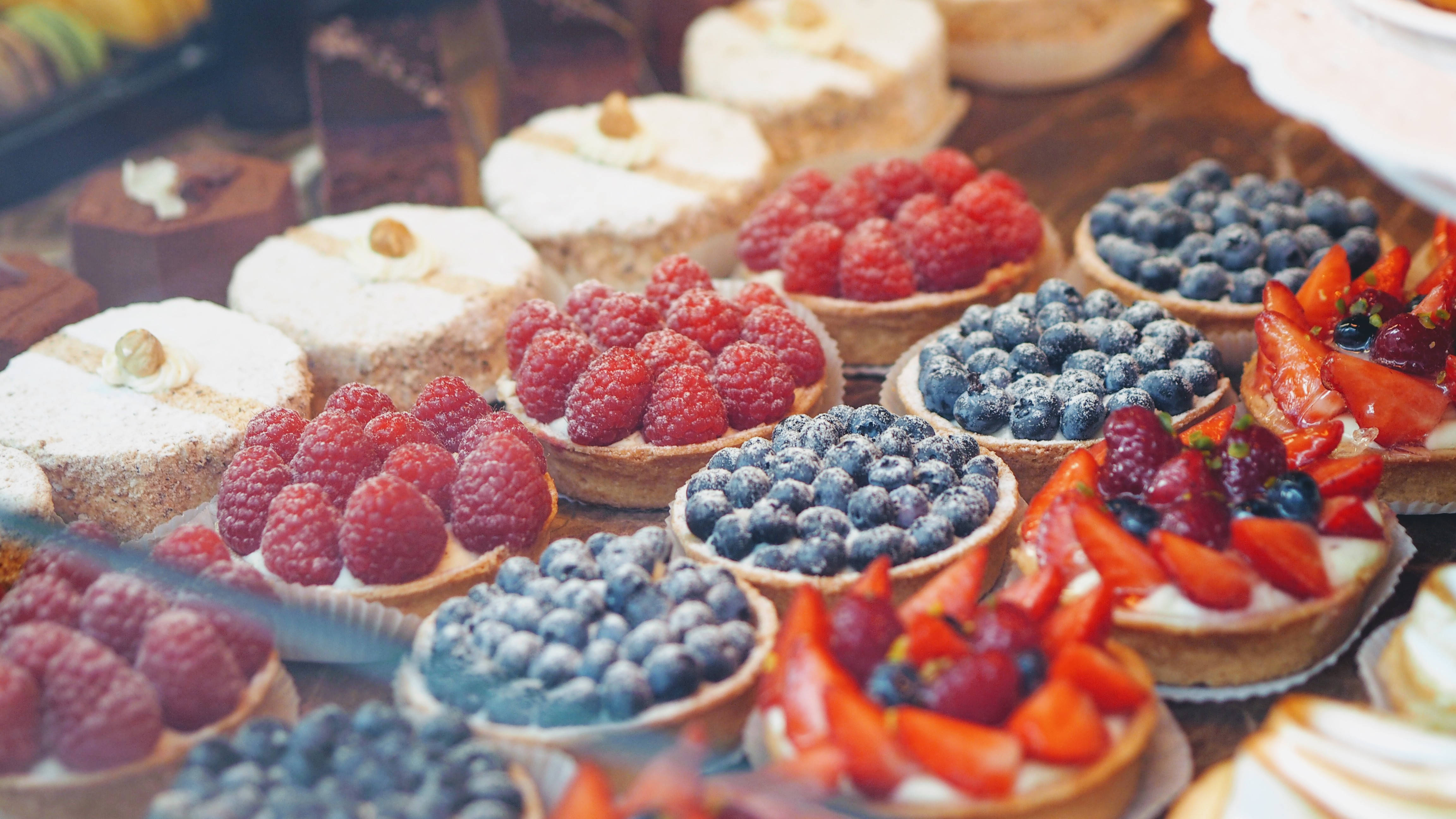 Pastry 桌布 壁紙 — 一個充滿活力的特寫鏡頭，展示木製陳列櫃上排列的各式水果撻和糕點。