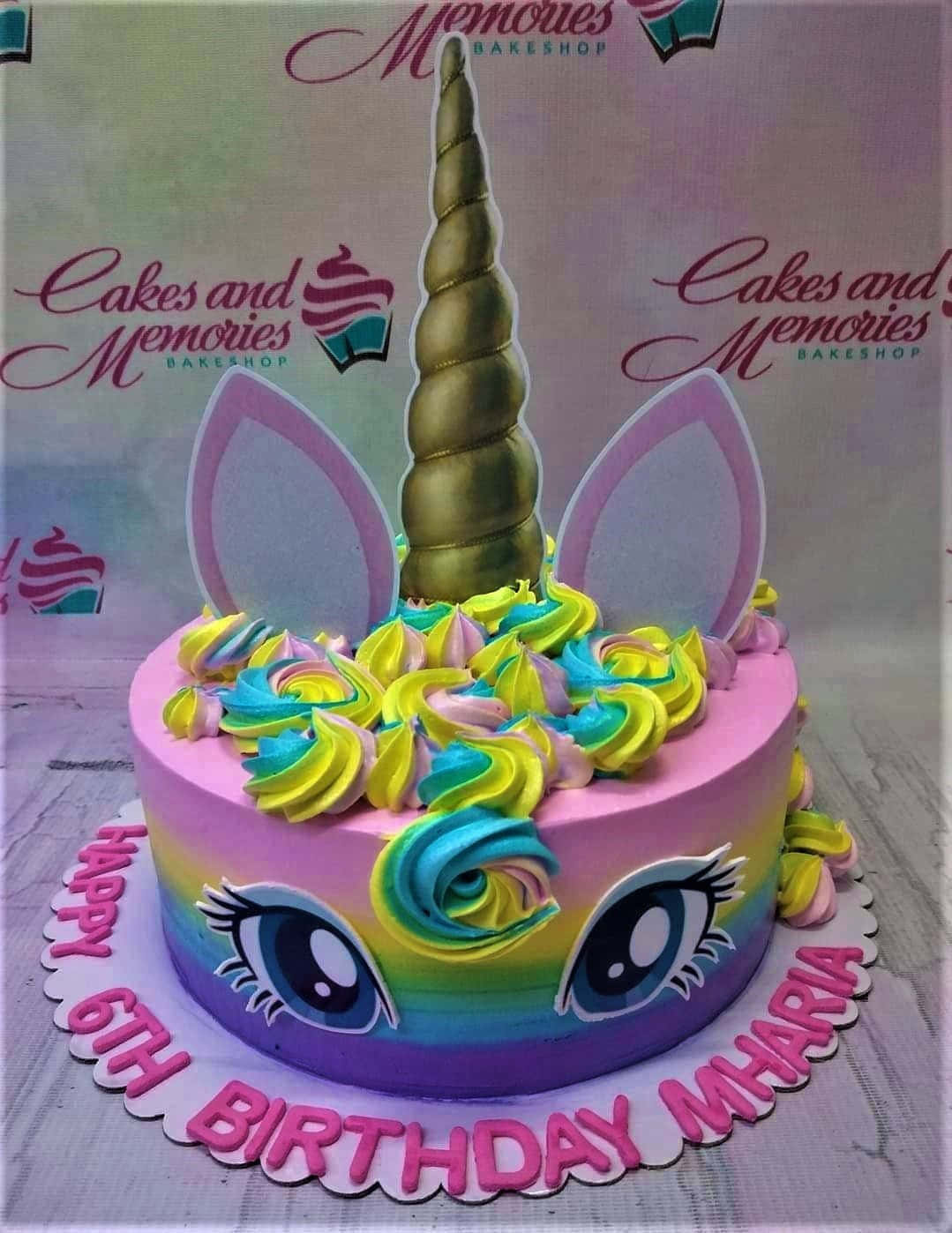 獨角獸 桌布 壁紙 — 一個充滿活力的獨角獸主題生日蛋糕，帶有彩虹糖霜眼睛和金色角，放在粉紅色扇貝形板上。