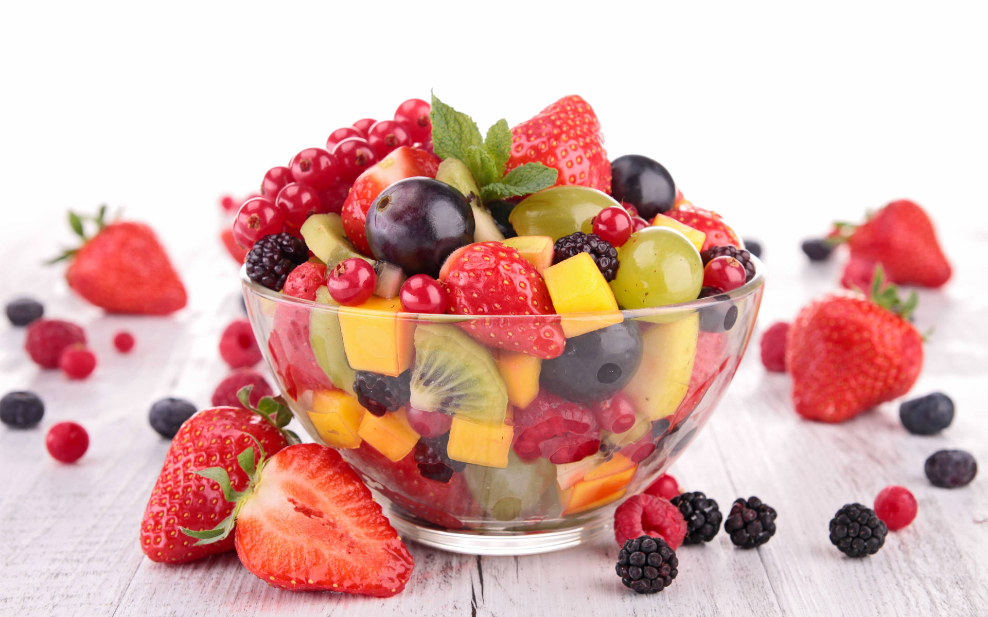 Berry 桌布 壁紙 — 一個充滿活力的玻璃碗，裝滿了色彩繽紛的切碎水果，如草莓、奇異果和葡萄，放在一個質樸的白色木質表面上。
