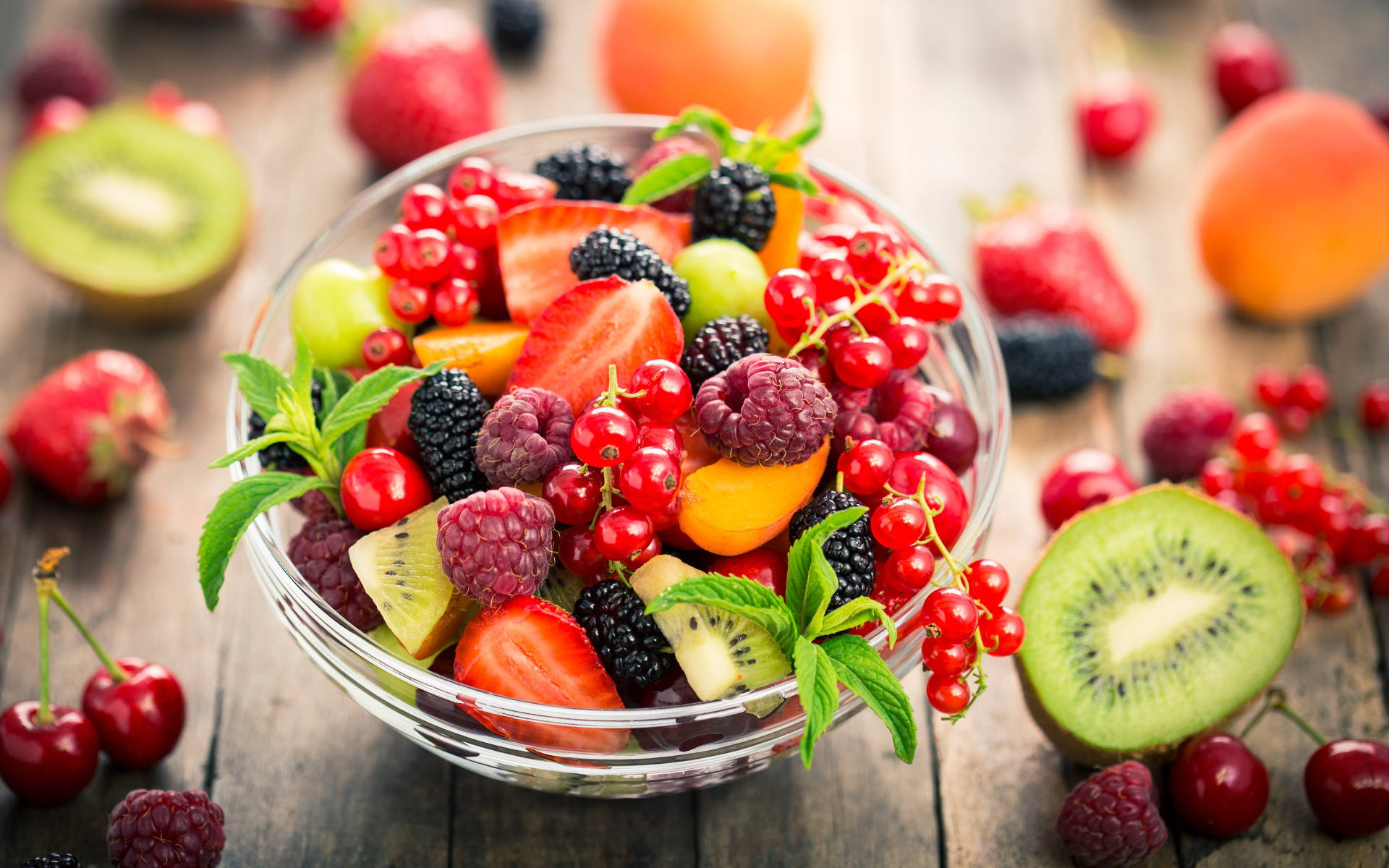 Berry 桌布 壁紙 — 一個充滿活力的玻璃碗，裝滿新鮮漿果、草莓、奇異果和櫻桃，放在質樸的木桌上。