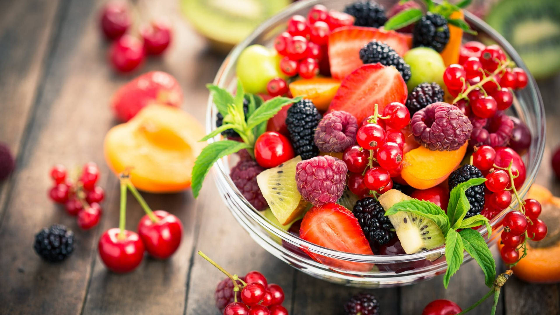 Berry 桌布 壁紙 — 一個充滿活力的玻璃碗，裝滿新鮮漿果、草莓、奇異果和櫻桃，放在質樸的木桌上。