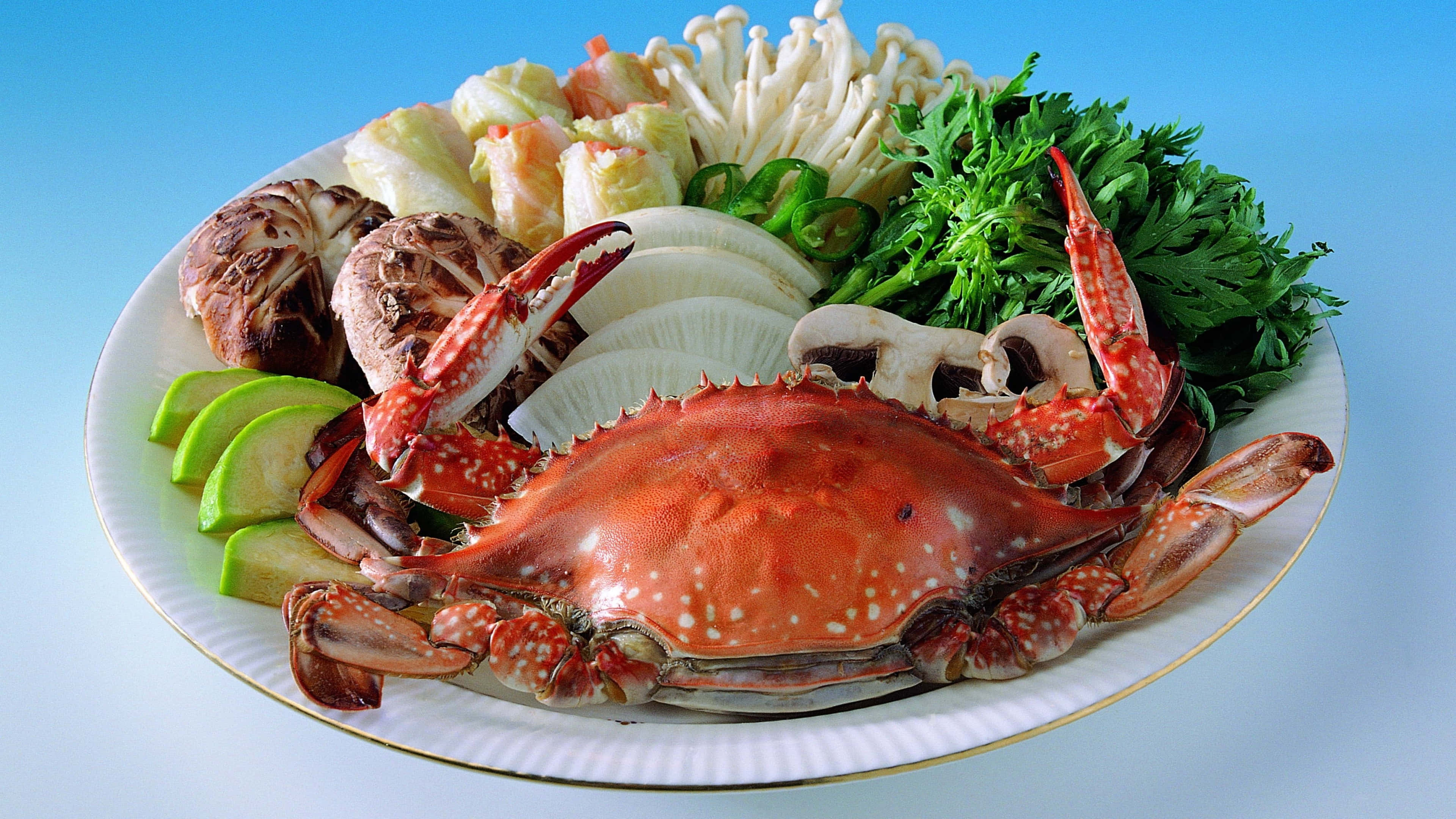 Seafood 桌布 壁紙 — 一個充滿活力的盤子，上面擺放著新鮮螃蟹和各種蔬菜，用於火鍋餐，背景為明亮的藍色。