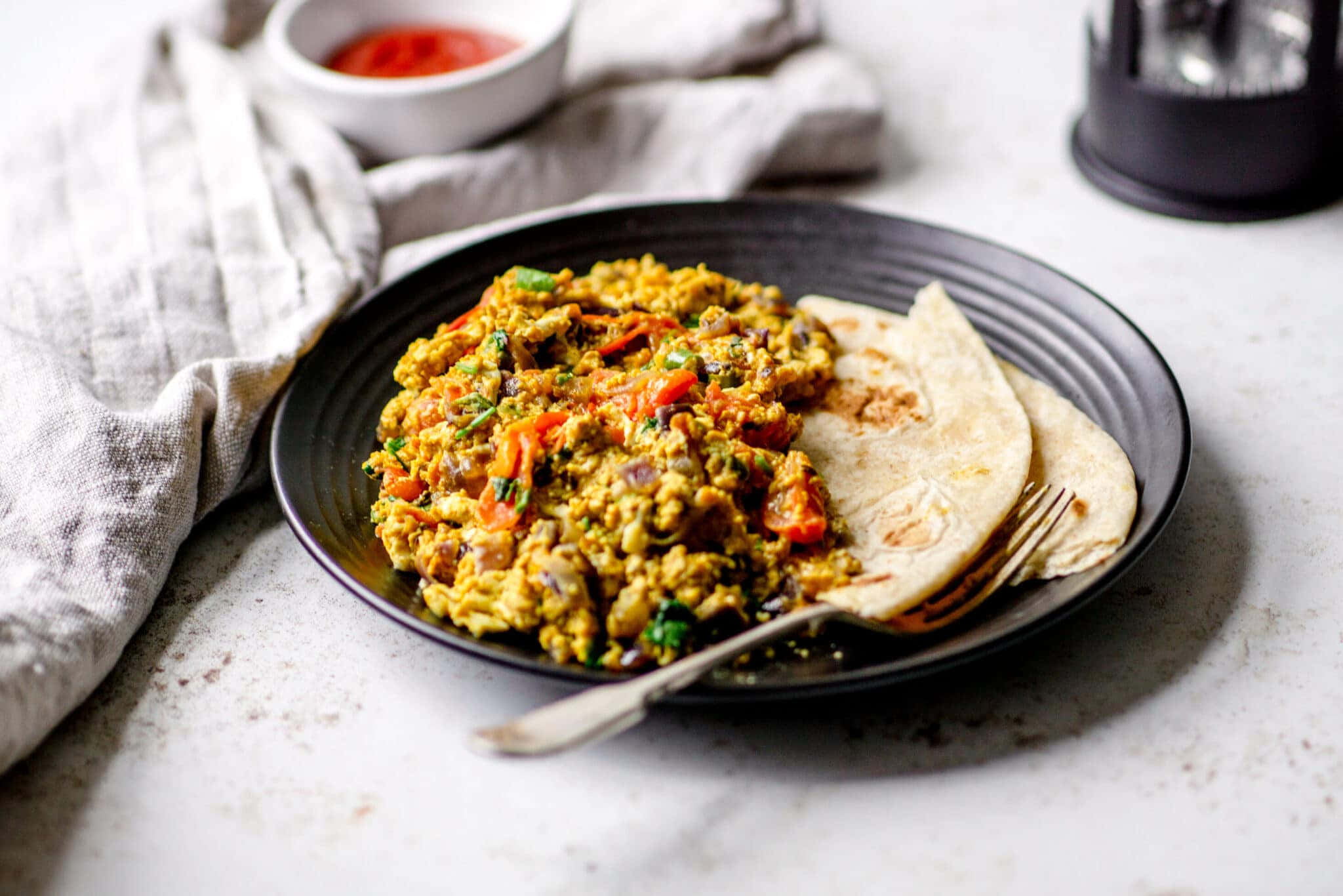 Scrambled Egg 桌布 壁紙 — 一個充滿活力的盤子，上面有香料炒豆腐、色彩繽紛的蔬菜和溫暖的玉米餅，放在簡約的白色檯面上。