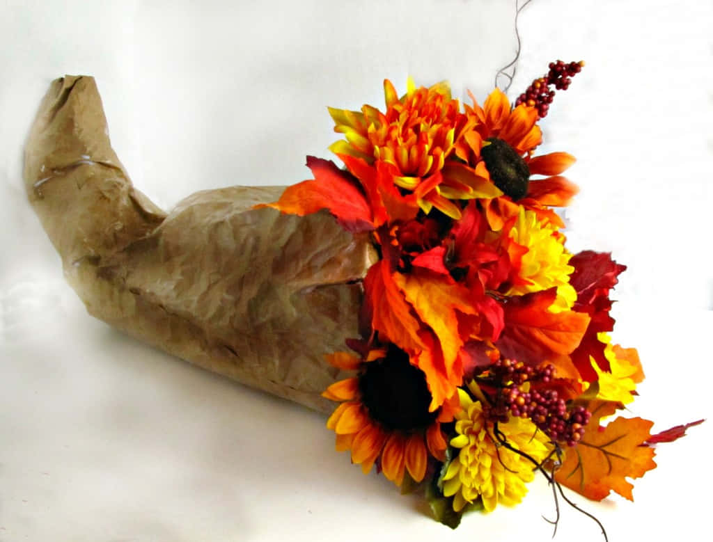 Fall Cornucopia 桌布 壁紙 — 一個充滿活力的秋季花卉佈置從一個皺巴巴的棕色紙質豐收角中溢出，背景是純白色。