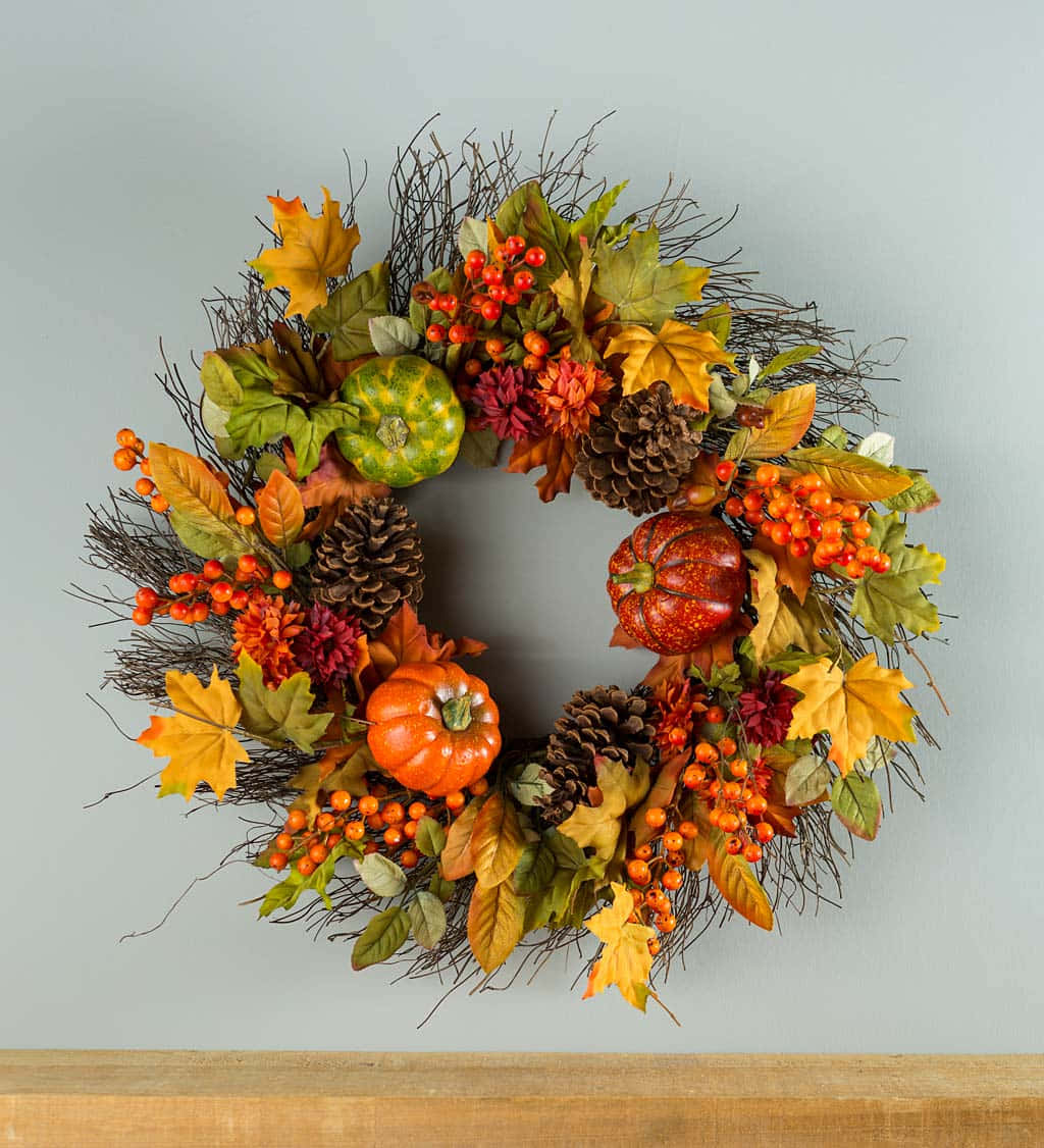 Fall Wreath 桌布 壁紙 — 一個充滿活力的秋季花環，裝飾著南瓜、松果、漿果和色彩繽紛的樹葉，掛在柔和的灰色牆上。