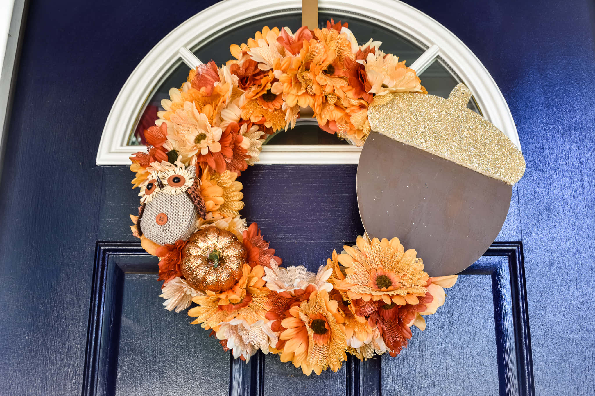 Fall Wreath 桌布 壁紙 — 一個充滿活力的秋季花環，飾有橙色花朵、閃閃發光的橡實和貓頭鷹裝飾，掛在深藍色的前門上。