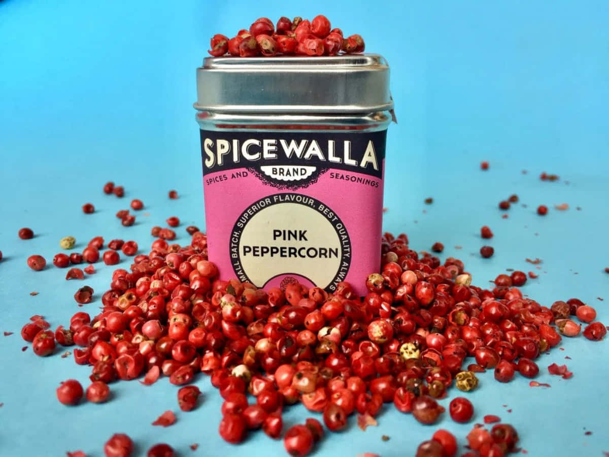 Pink Peppercorn 桌布 壁紙 — 一個充滿活力的粉紅胡椒罐，裝滿鮮紅色的莓果，襯著純藍色背景。