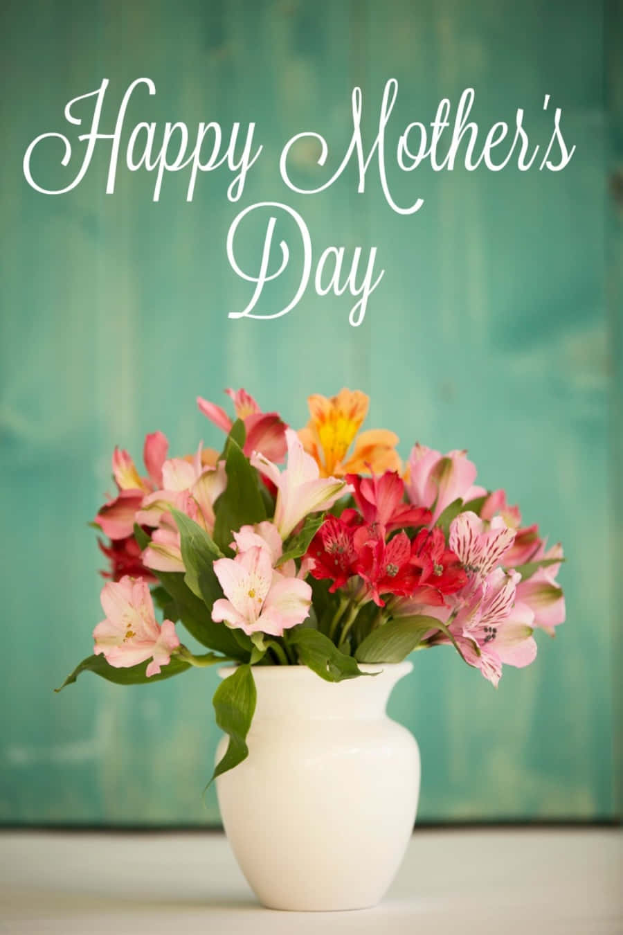 Happy Mothers Day 桌布 壁紙 — 一個充滿活力的粉紅色、紅色和橙色六出花束，放在白色花瓶裡，背景是藍綠色木質，上方寫有「Happy Mother's Day」。