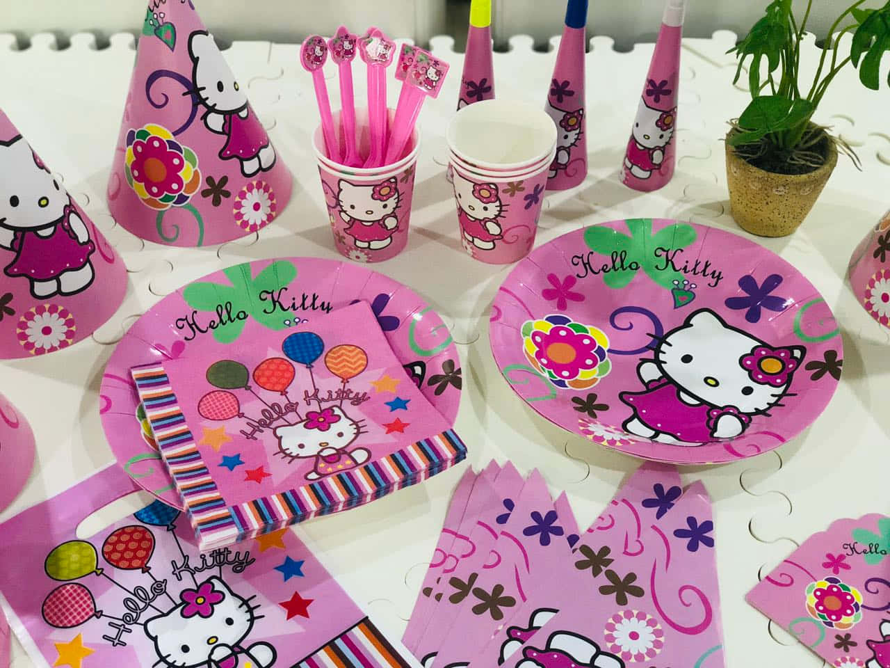 Hello Kitty Party 桌布 壁紙 — 一個充滿活力的粉紅色Hello Kitty派對擺設，包括盤子、杯子和帽子，排列在白色表面上。