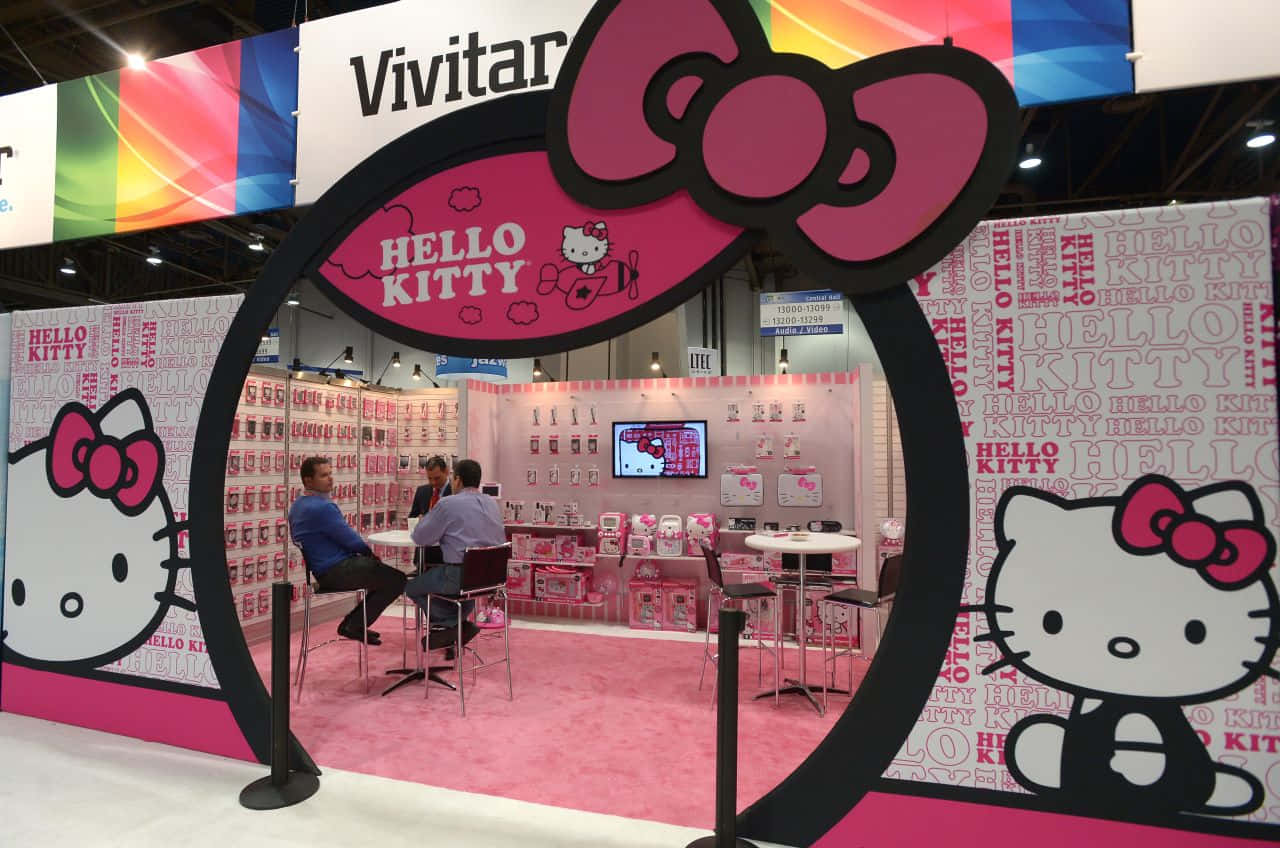 Hello Kitty 桌布 壁紙 — 一個充滿活力的粉紅色Hello Kitty品牌展位，設有大型角色剪影和瀏覽產品的參觀者。