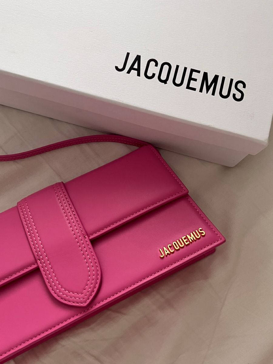 Handbag 桌布 壁紙 — 一個充滿活力的粉紅色Jacquemus錢包放在其品牌白色盒子旁邊，置於柔軟的米色表面上。
