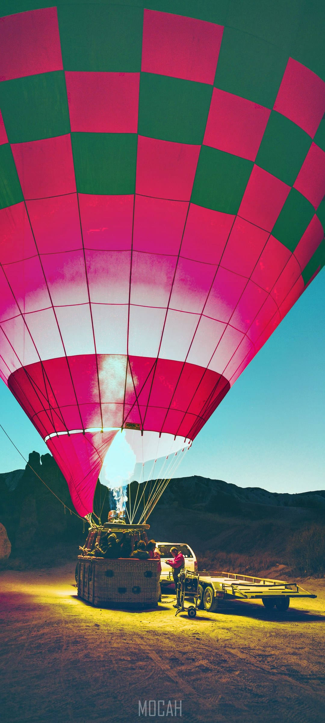 Cappadocia 桌布 壁紙 — 一個充滿活力的粉紅色和綠色格子熱氣球在日出時分，以沙漠峽谷為背景充氣。