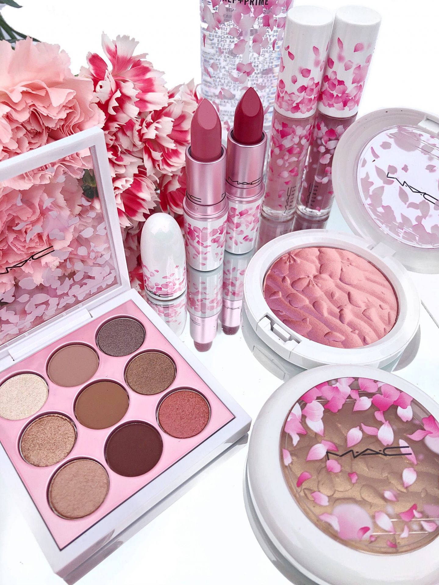 Cosmetics 桌布 壁紙 — 一個充滿活力的粉紅色櫻花主題MAC化妝品系列，與新鮮康乃馨一起展示在反光的白色表面上。