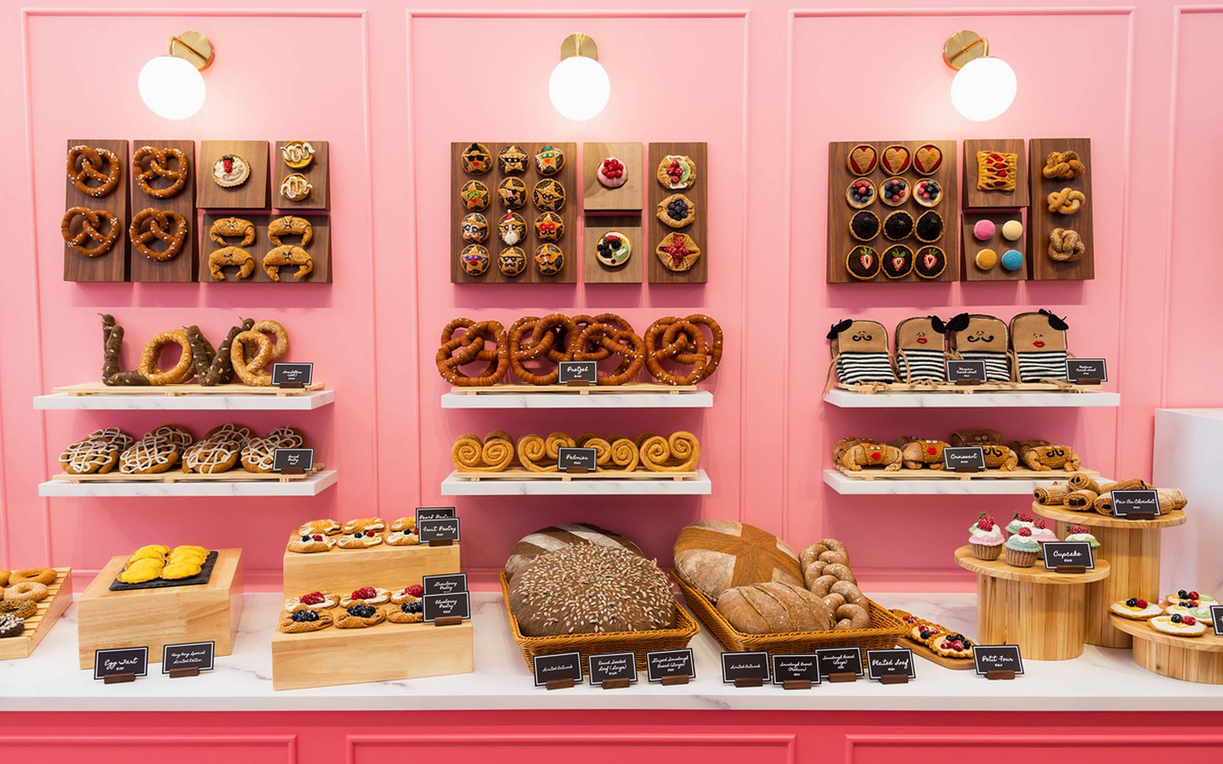 Bakery 桌布 壁紙 — 一個充滿活力的粉紅色烘焙展示櫃，整齊地陳列著各種糕點、蝴蝶結麵包和麵包，放在木架和大理石檯面上。