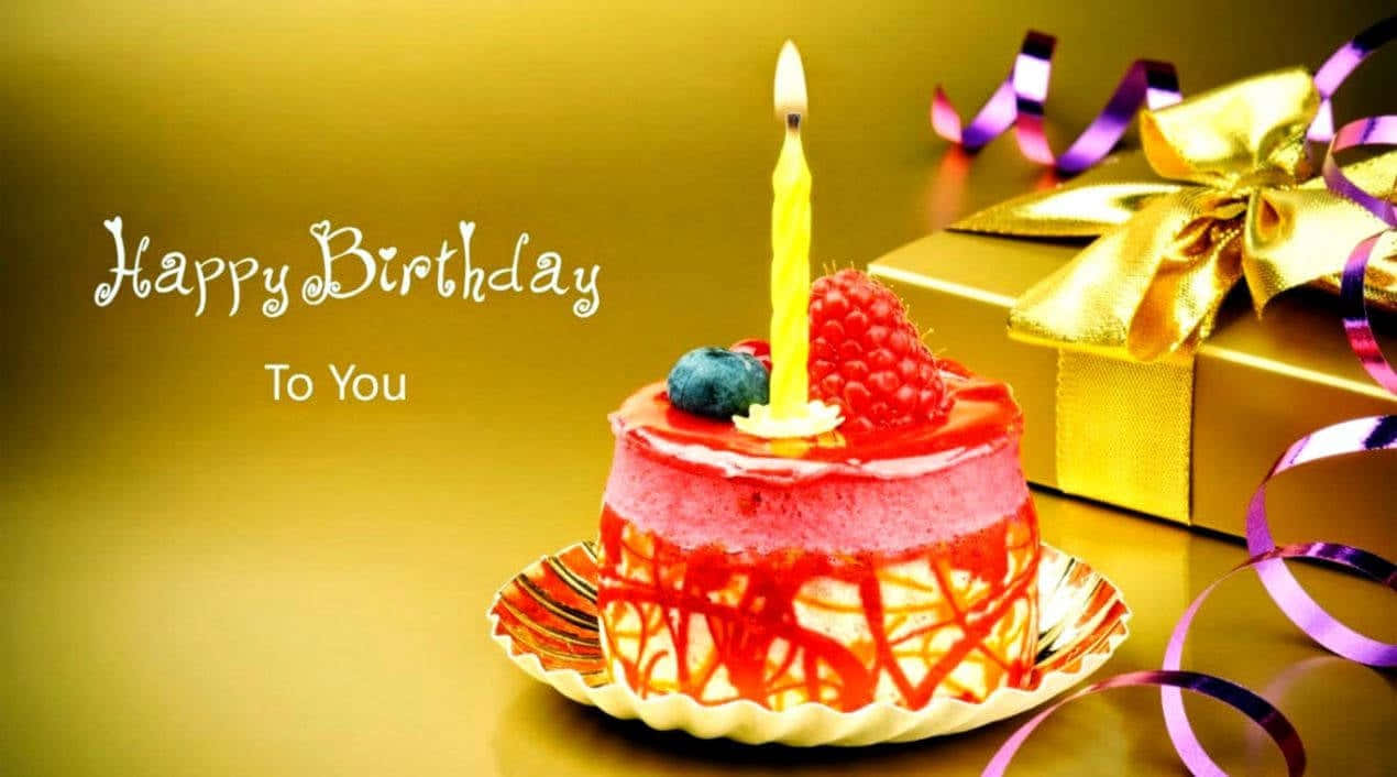 Birthday 桌布 壁紙 — 一個充滿活力的粉紅色生日蛋糕，上面有一根點燃的蠟燭和新鮮漿果，旁邊是一個金色禮物盒，飾有紫色絲帶。