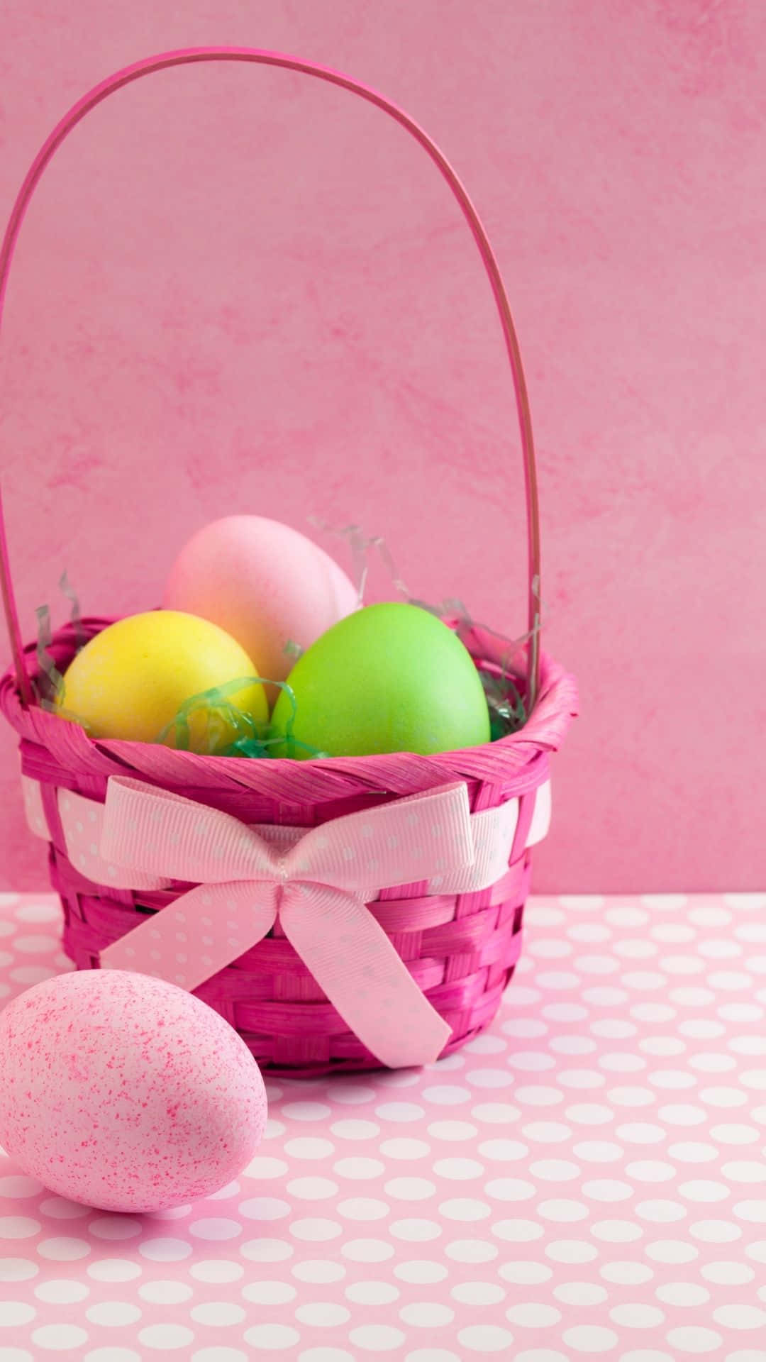 Easter Basket 桌布 壁紙 — 一個充滿活力的粉紅色編織籃子，飾有絲帶，在相配的粉紅色紋理背景上盛放著色彩繽紛的復活節彩蛋。