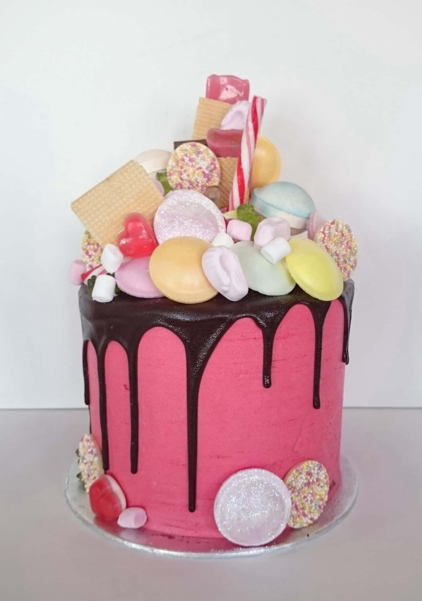Cake Fondant 桌布 壁紙 — 一個充滿活力的粉紅色蛋糕，上面有巧克力滴落和色彩繽紛的糖果和餅乾堆疊。