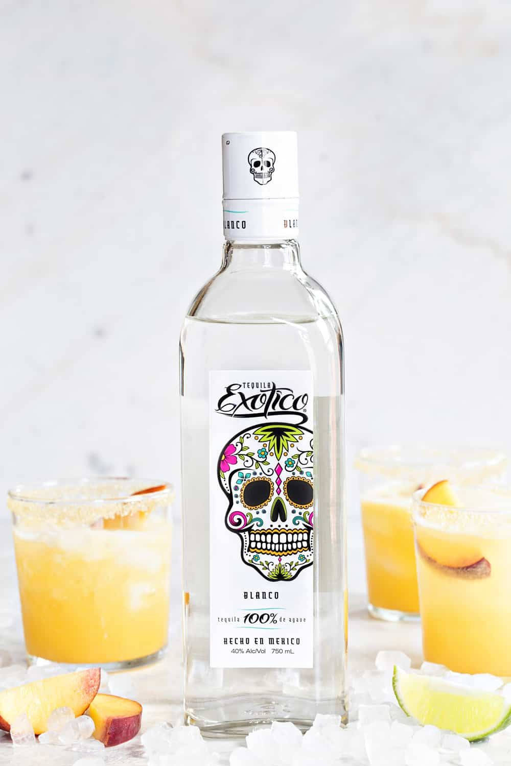 cocktail 桌布 壁紙 — 一個充滿活力的糖骷髏龍舌蘭酒瓶矗立在中央，旁邊是桃子瑪格麗特和萊姆角，放在冰床上。
