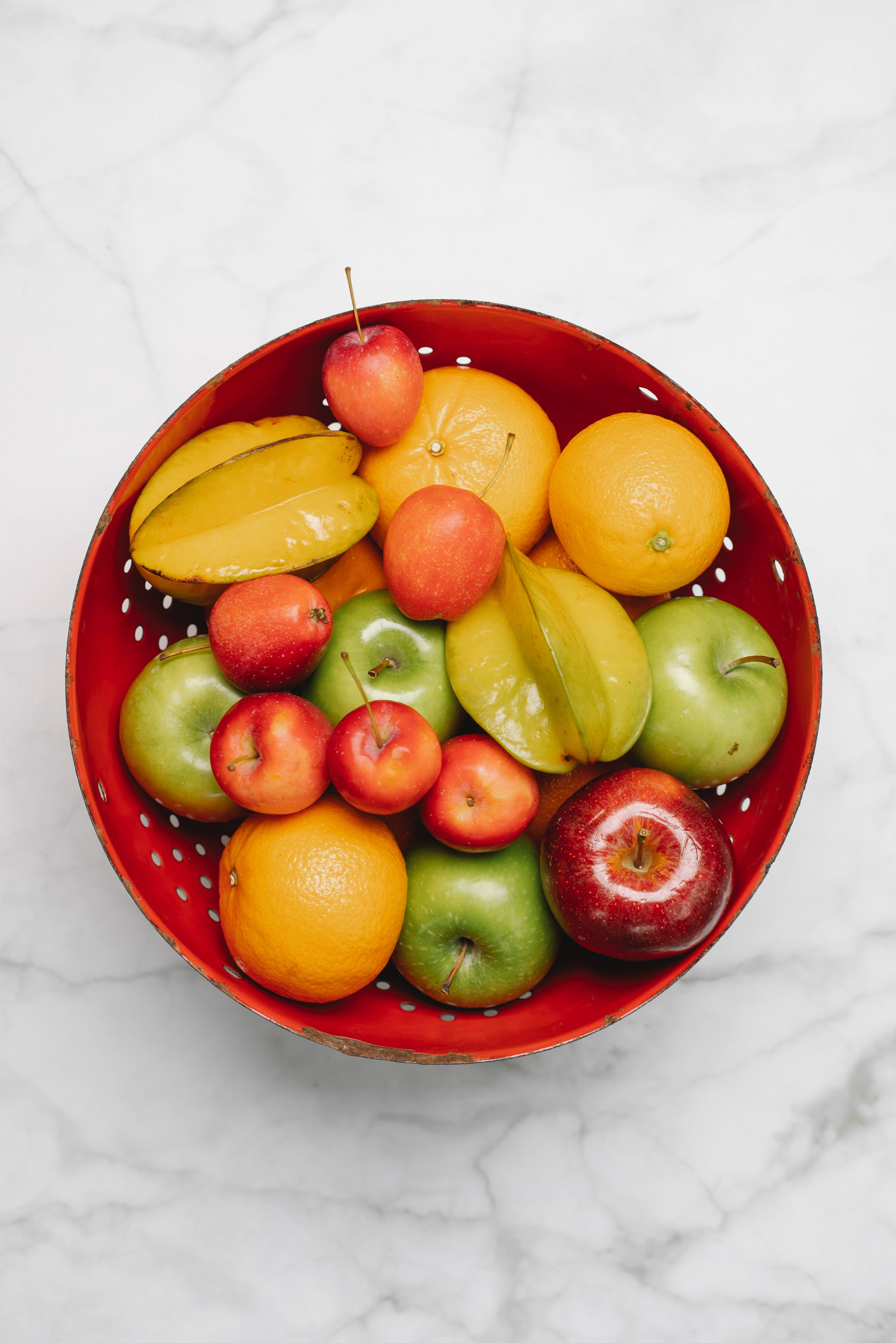 Fruit 桌布 壁紙 — 一個充滿活力的紅色濾器，裝滿了各種新鮮水果，包括蘋果、柳橙和楊桃，放在白色大理石表面上。