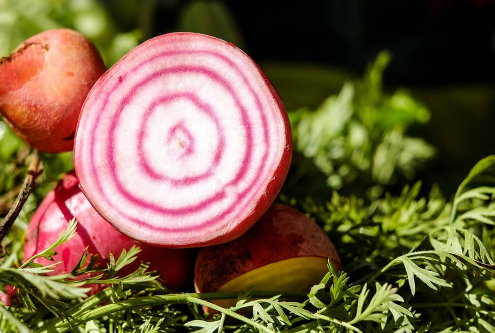 beetroot 桌布 壁紙 — 一個充滿活力的紅菜頭橫切面，揭示了新鮮綠色香草中錯綜複雜的粉紅色和白色同心環。