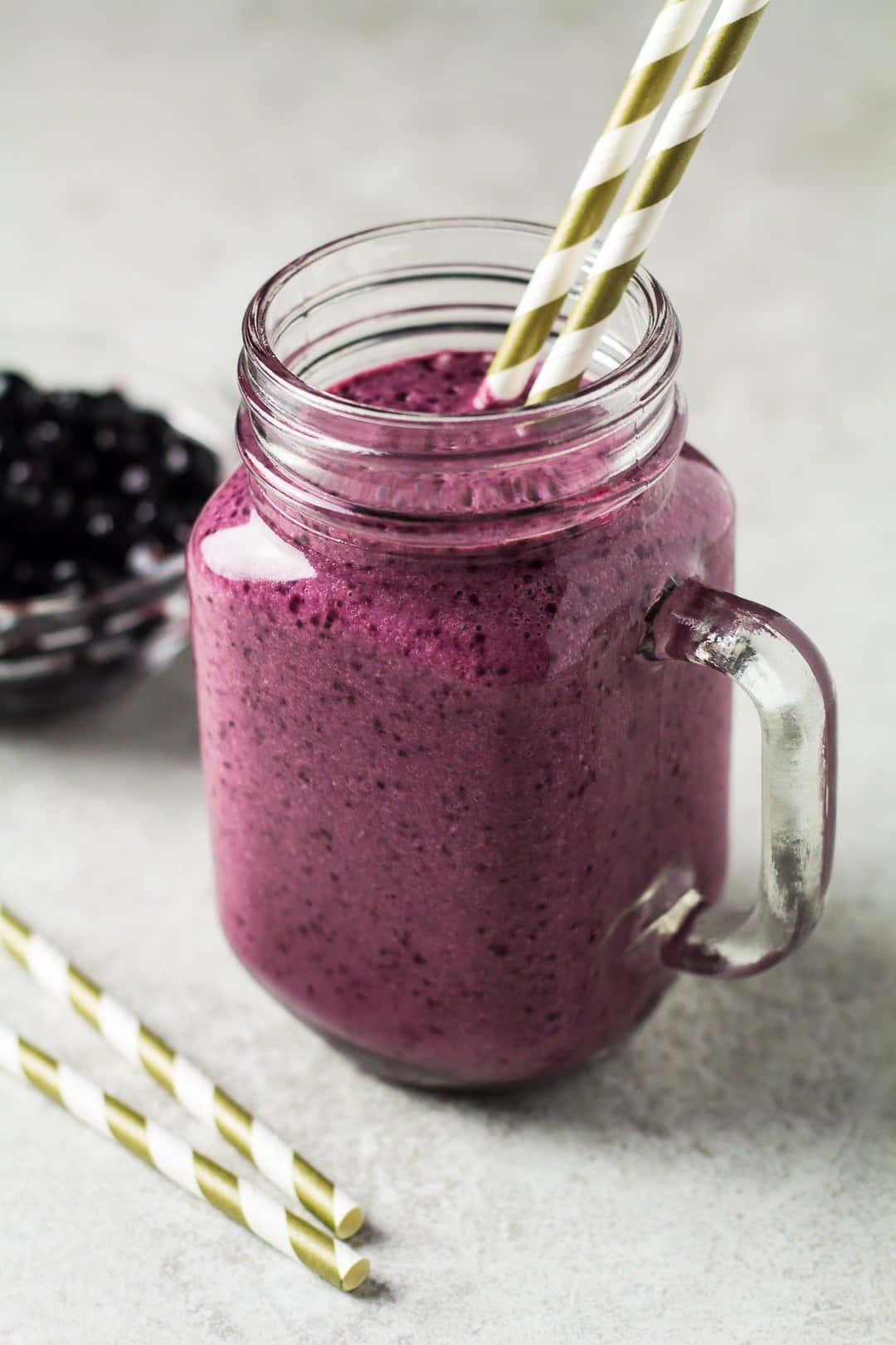 Blueberry Smoothie 桌布 壁紙 — 一個充滿活力的紫色冰沙放在玻璃梅森罐中，配有金色和白色條紋吸管，旁邊還有新鮮的黑莓。