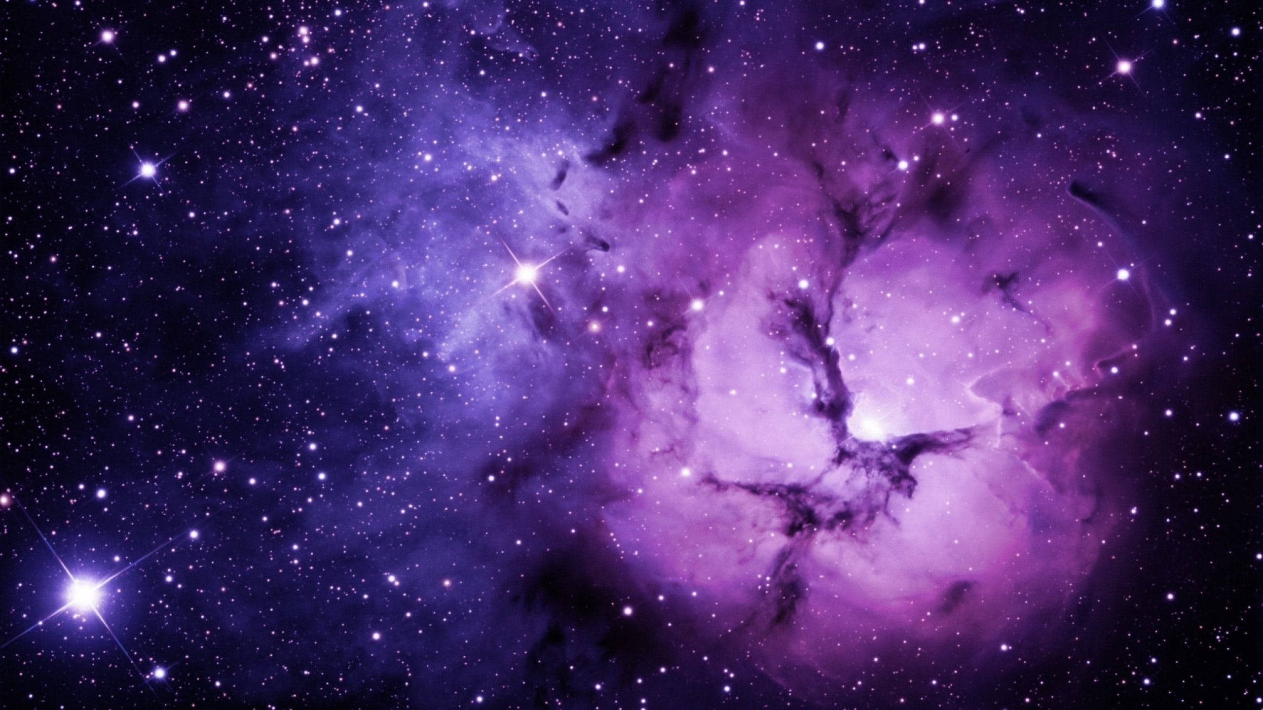 黑色與紫色 桌布 壁紙 — 一個充滿活力的紫色星雲，在深邃的宇宙虛空中，旋轉著發光的氣體和散落的明亮星星。