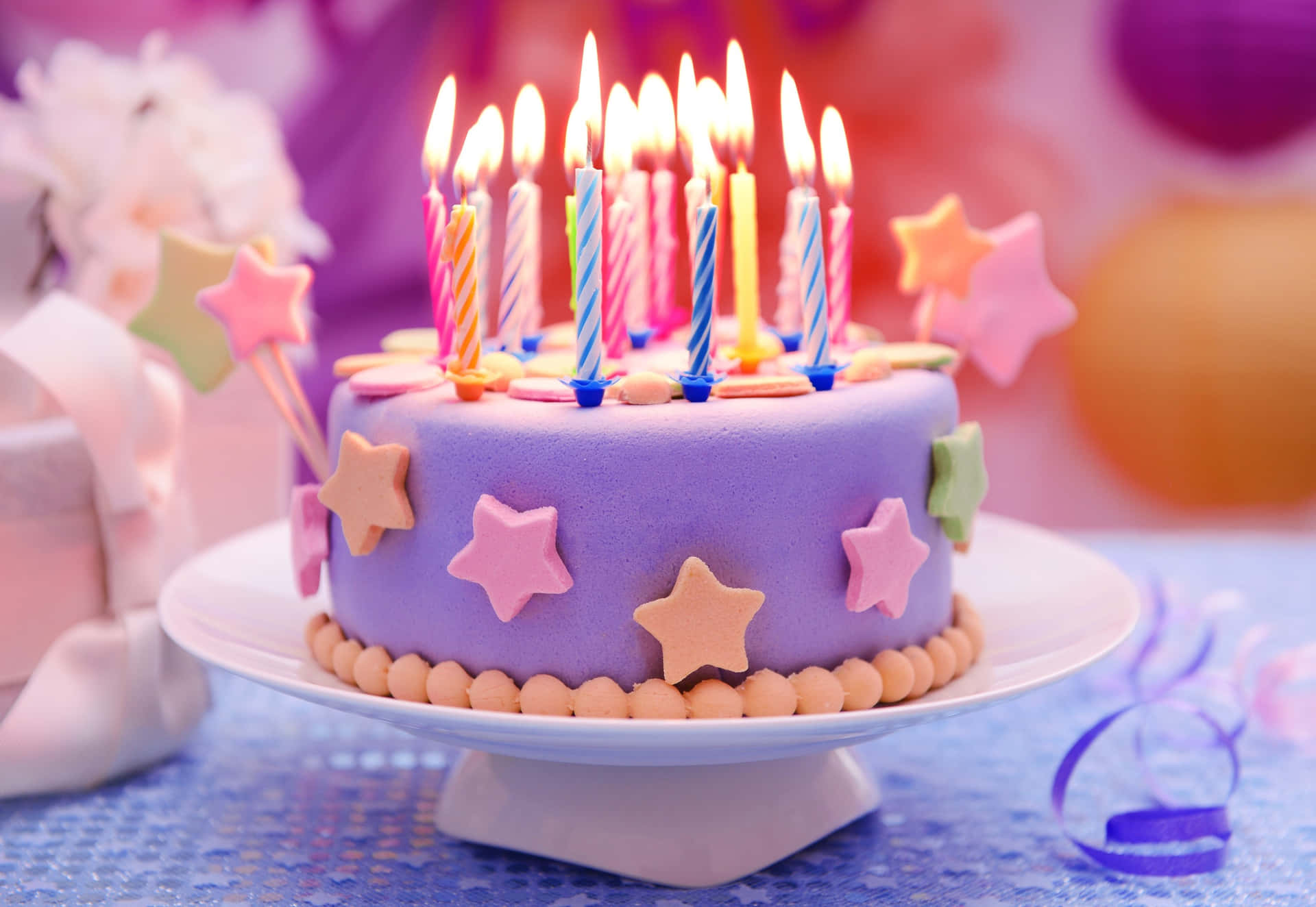  壁紙 — 一個充滿活力的紫色生日蛋糕，飾有彩色蠟燭和星形裝飾，在節日模糊的背景中溫暖地閃耀。