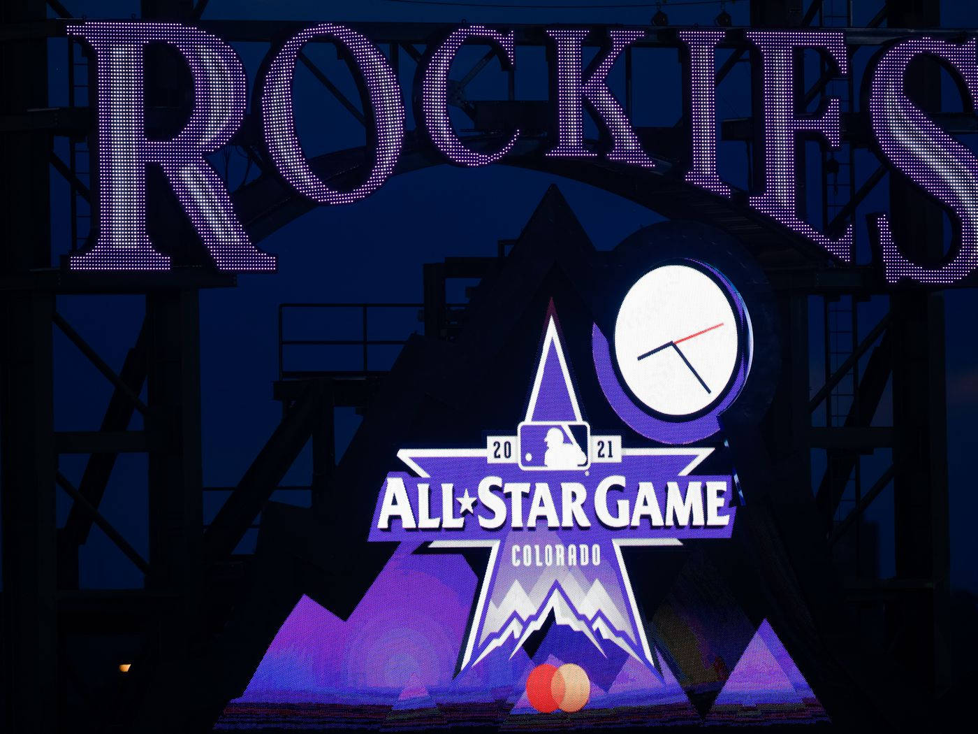 Rockies 桌布 壁紙 — 一個充滿活力的紫色發光洛磯隊全明星賽標誌，在黑暗的夜空中閃耀，帶有時鐘和山脈標誌。