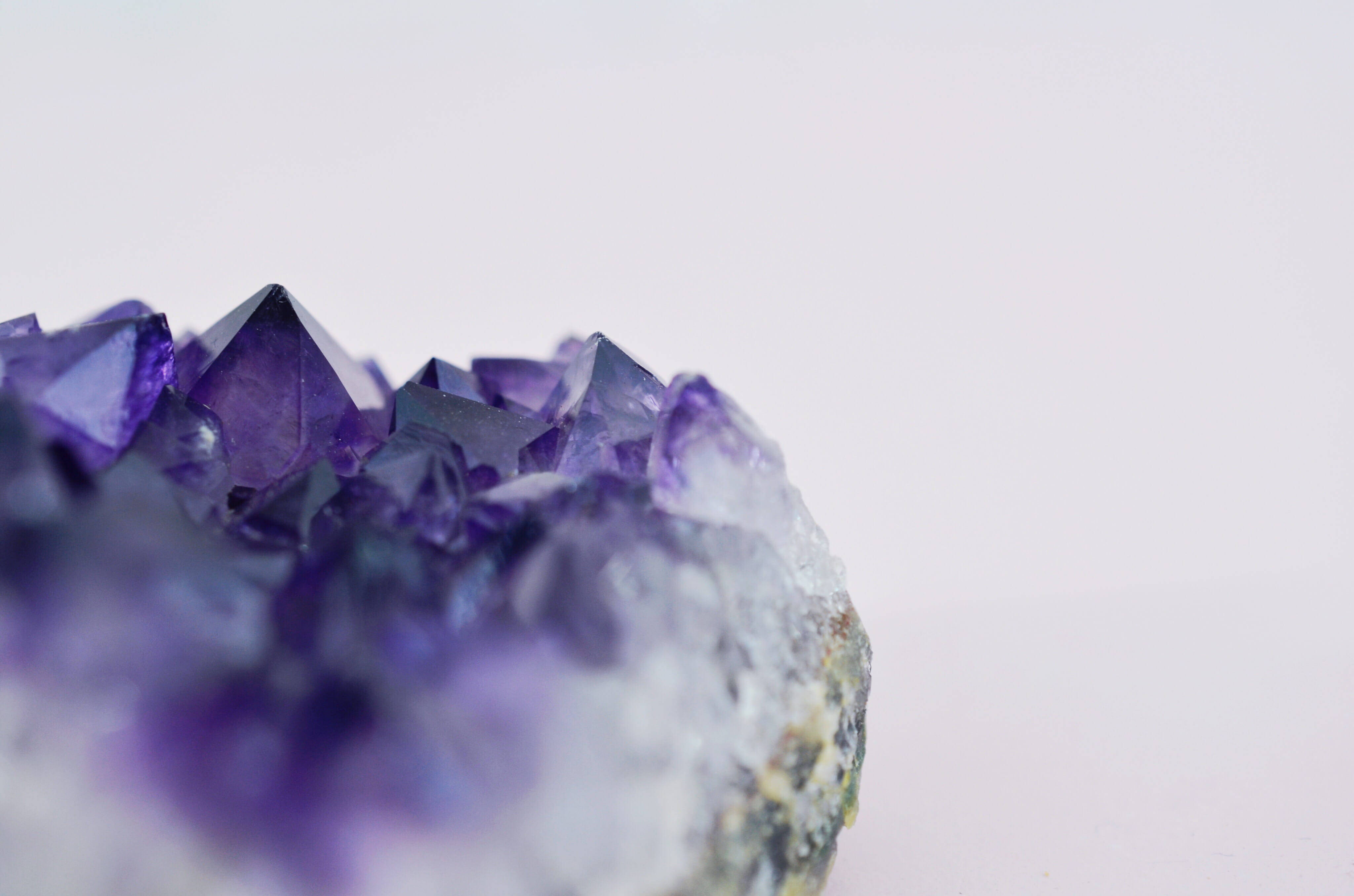 Amethyst 桌布 壁紙 — 一個充滿活力的紫色紫水晶晶體簇的特寫，具有銳利的切面，背景為柔和的白色。