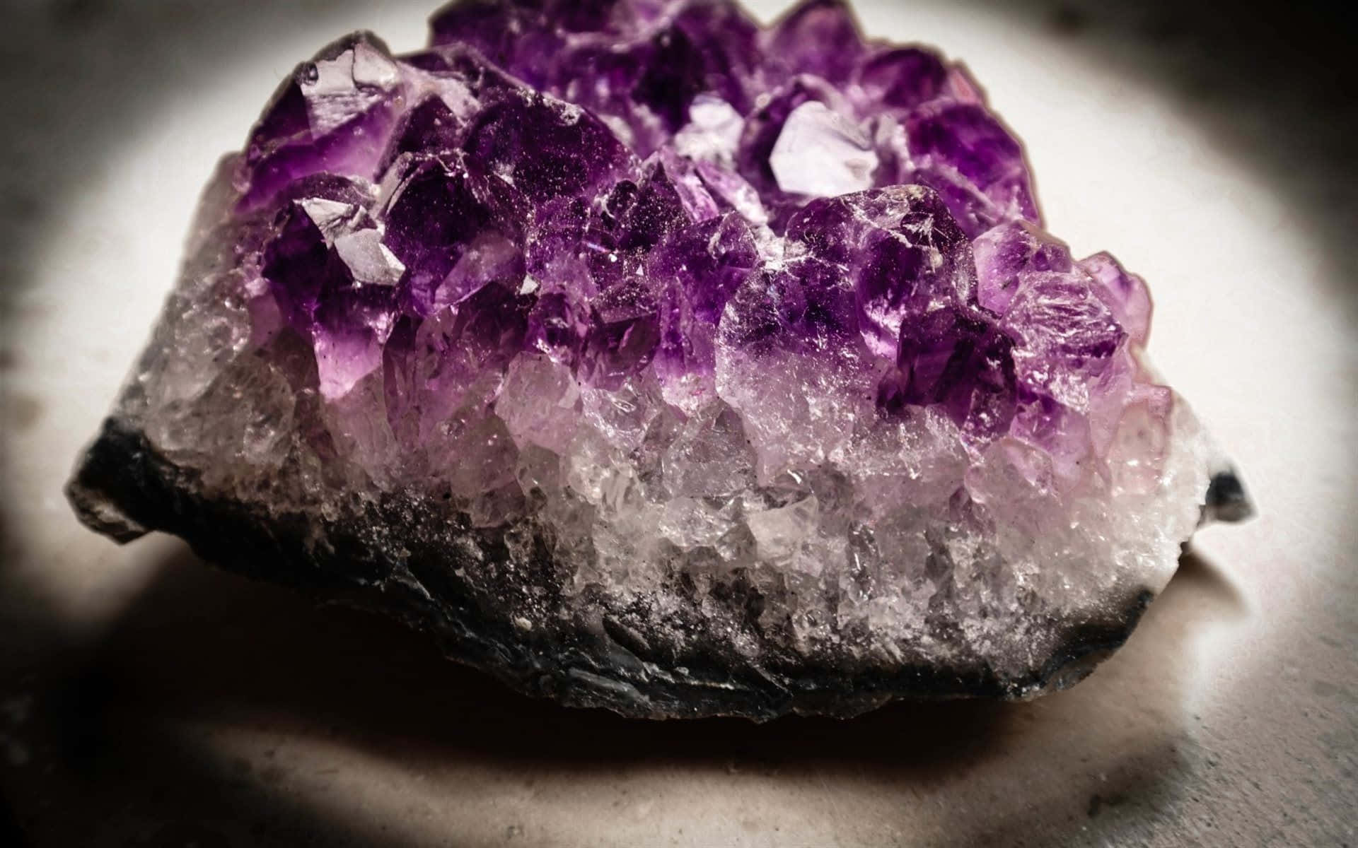 紫水晶 桌布 壁紙 — 一個充滿活力的紫色紫水晶晶體簇的特寫，具有清晰的切面和深色底座，由柔和的定向光照明。
