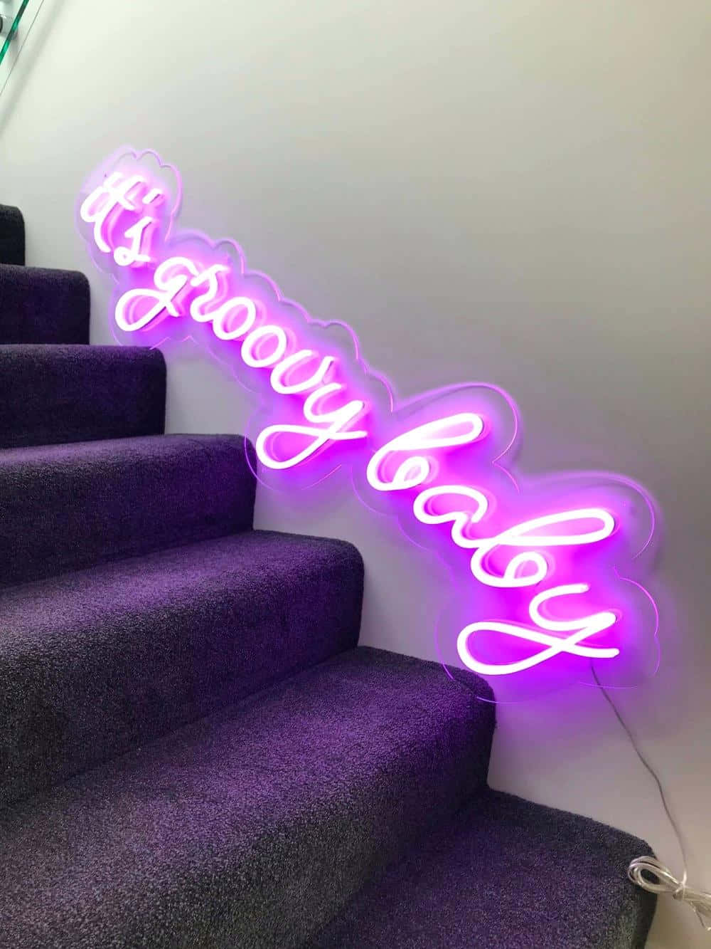 Neon Aesthetic Phone 桌布 壁紙 — 一個充滿活力的紫色霓虹燈牌，上面寫著「it's groovy baby」，在現代室內鋪有地毯的樓梯上方閃耀。