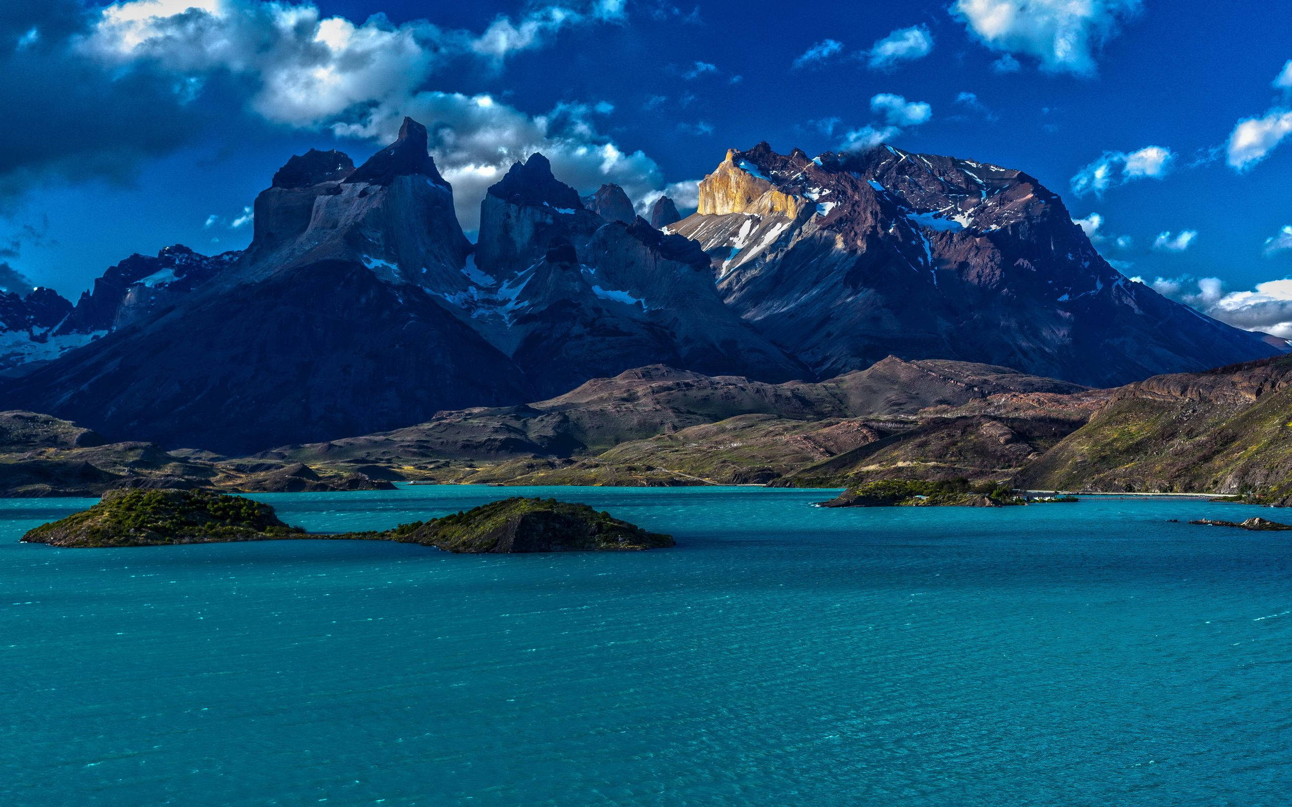 Patagonia 桌布 壁紙 — 一個充滿活力的綠松石色湖泊映照著崎嶇的雪山，在蔚藍的天空下，點綴著蓬鬆的白雲。