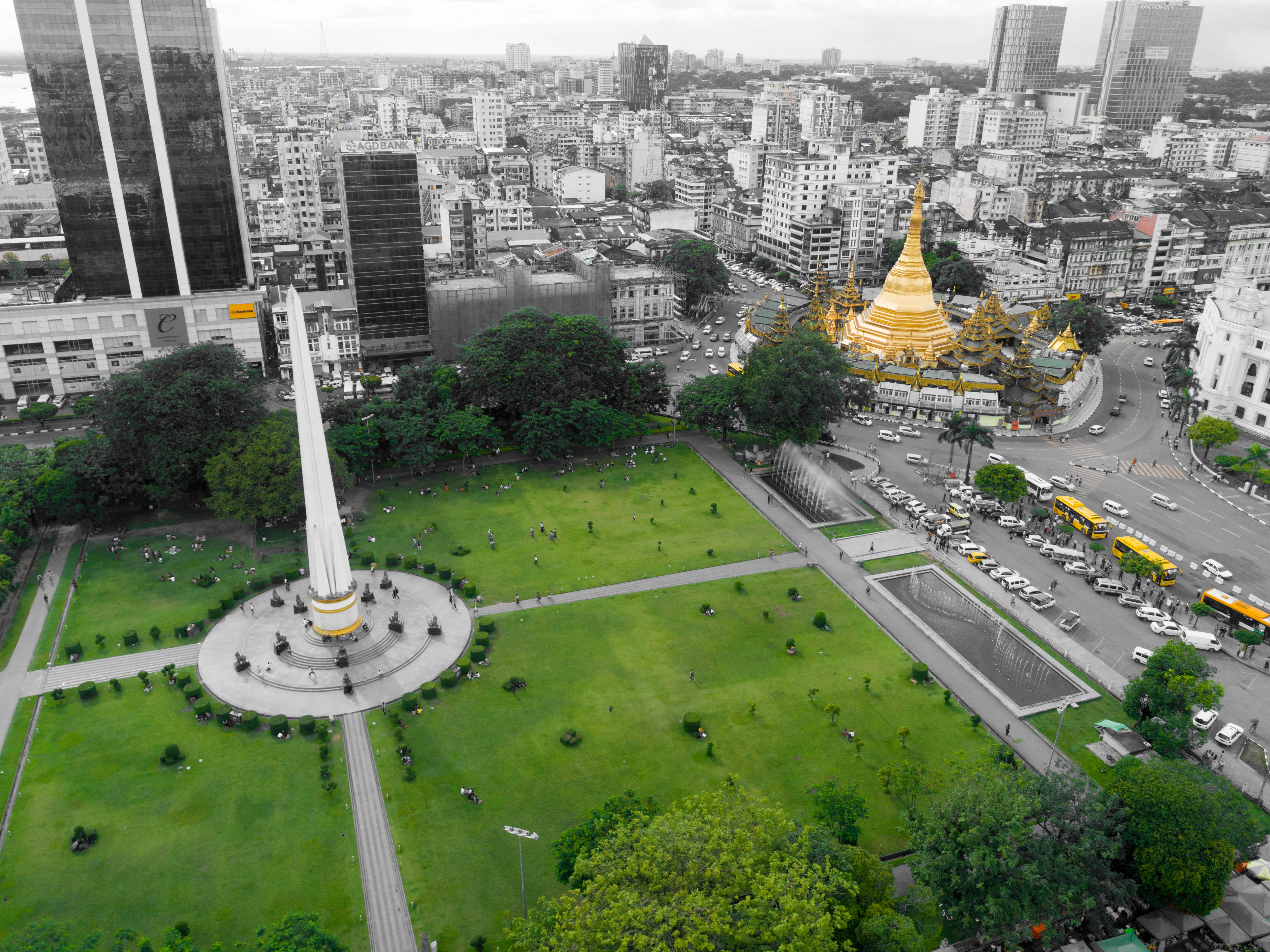 Yangon 桌布 壁紙 — 一個充滿活力的綠色公園的鳥瞰圖，一座高大的白色紀念碑被繁華的城市景觀和金色寶塔所環繞。