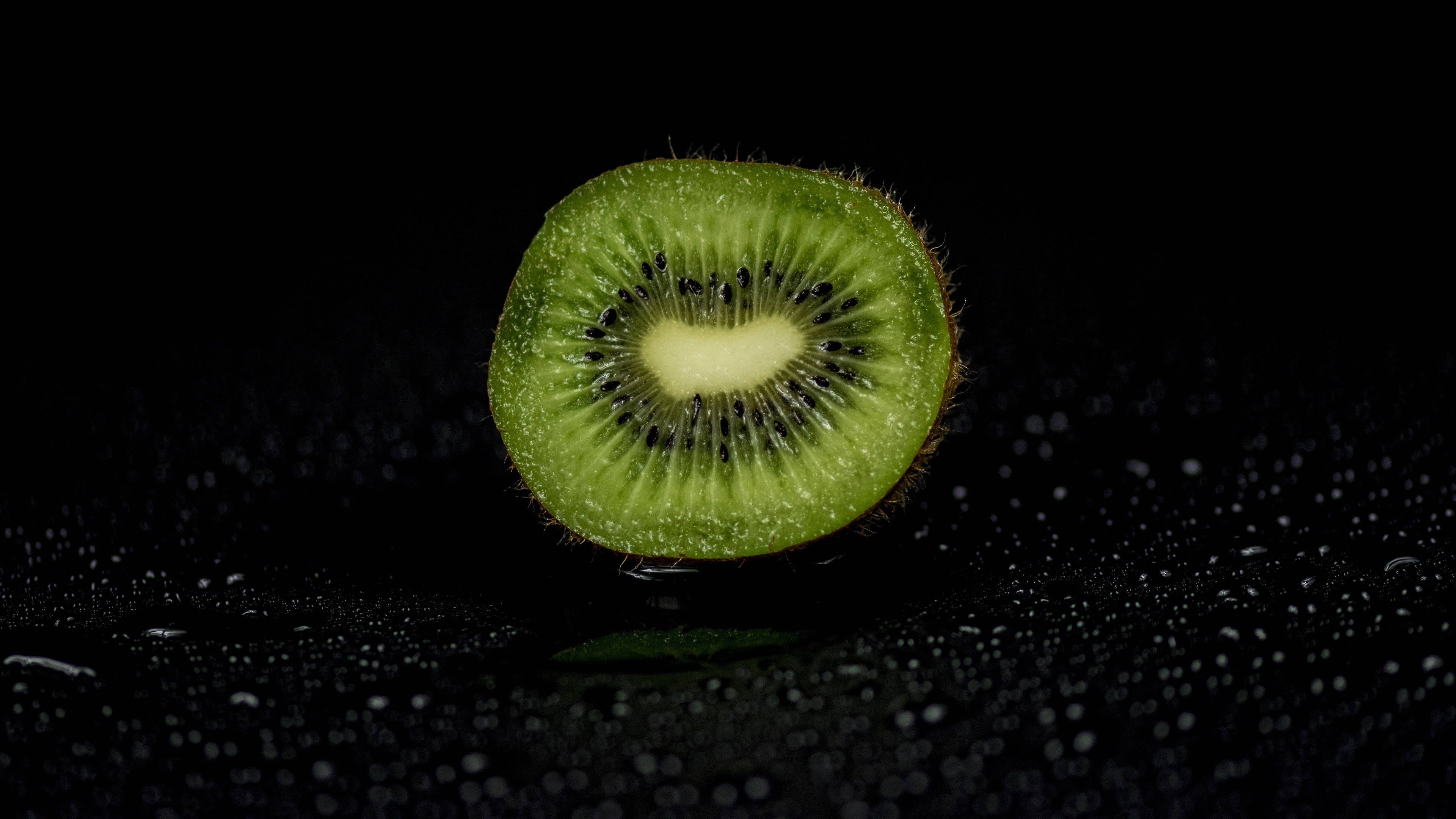 Fruits 桌布 壁紙 — 一個充滿活力的綠色奇異果切成兩半，放在潮濕的黑色表面上，水滴反射光線。